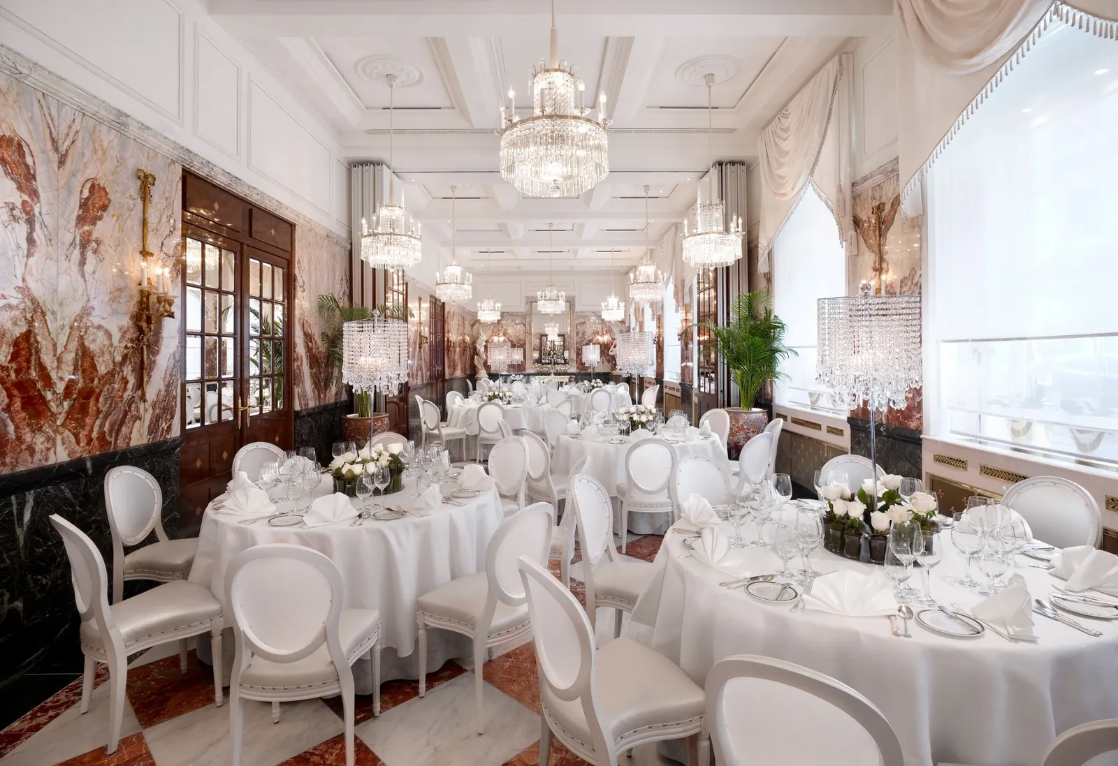 The Marble Hall laid with round white-clothed tables: veined marble walls, crystal chandeliers and white chairs.