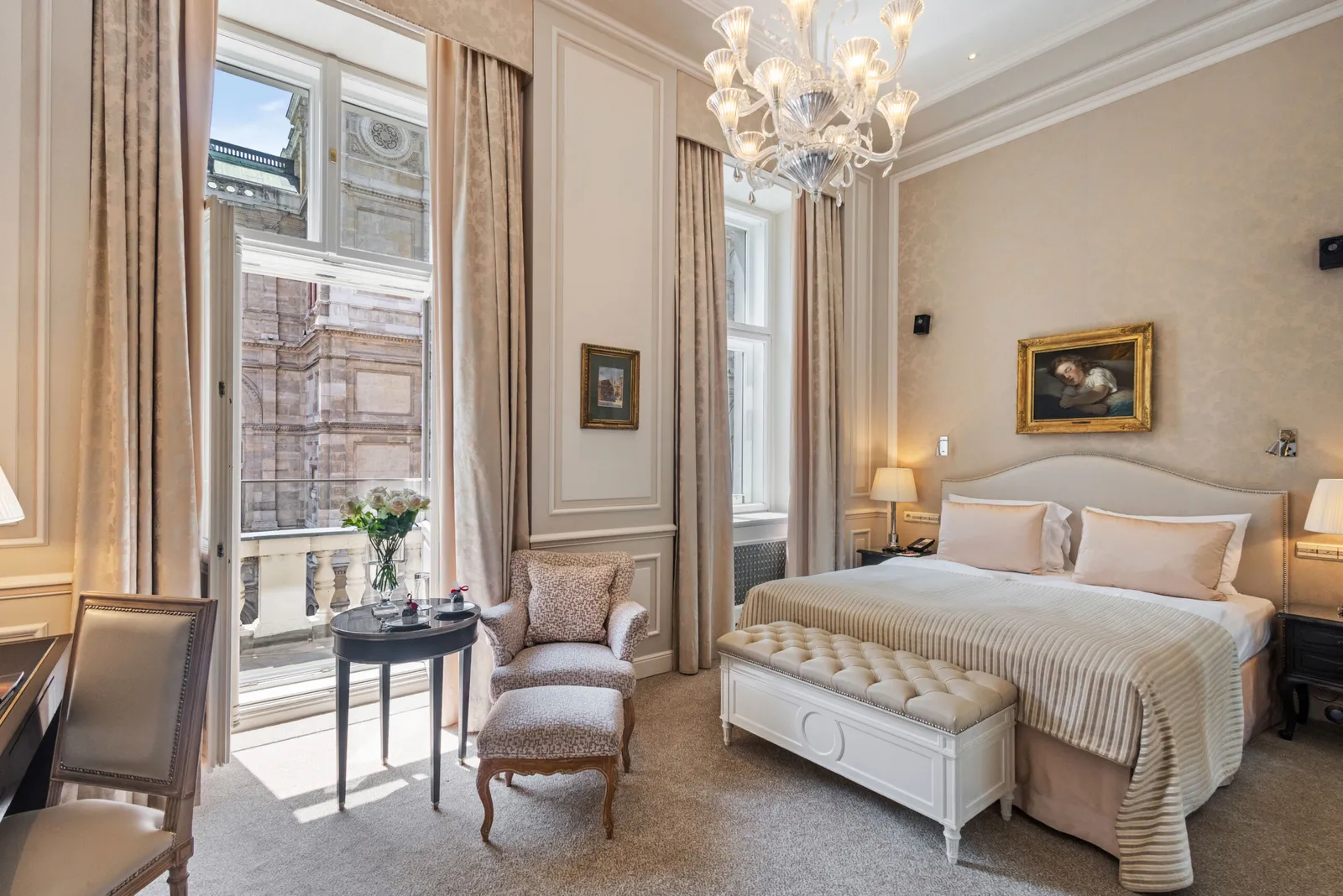 A Deluxe Room with View: the double bed, a crystal chandelier and the French window open on a balcony facing the State Opera.