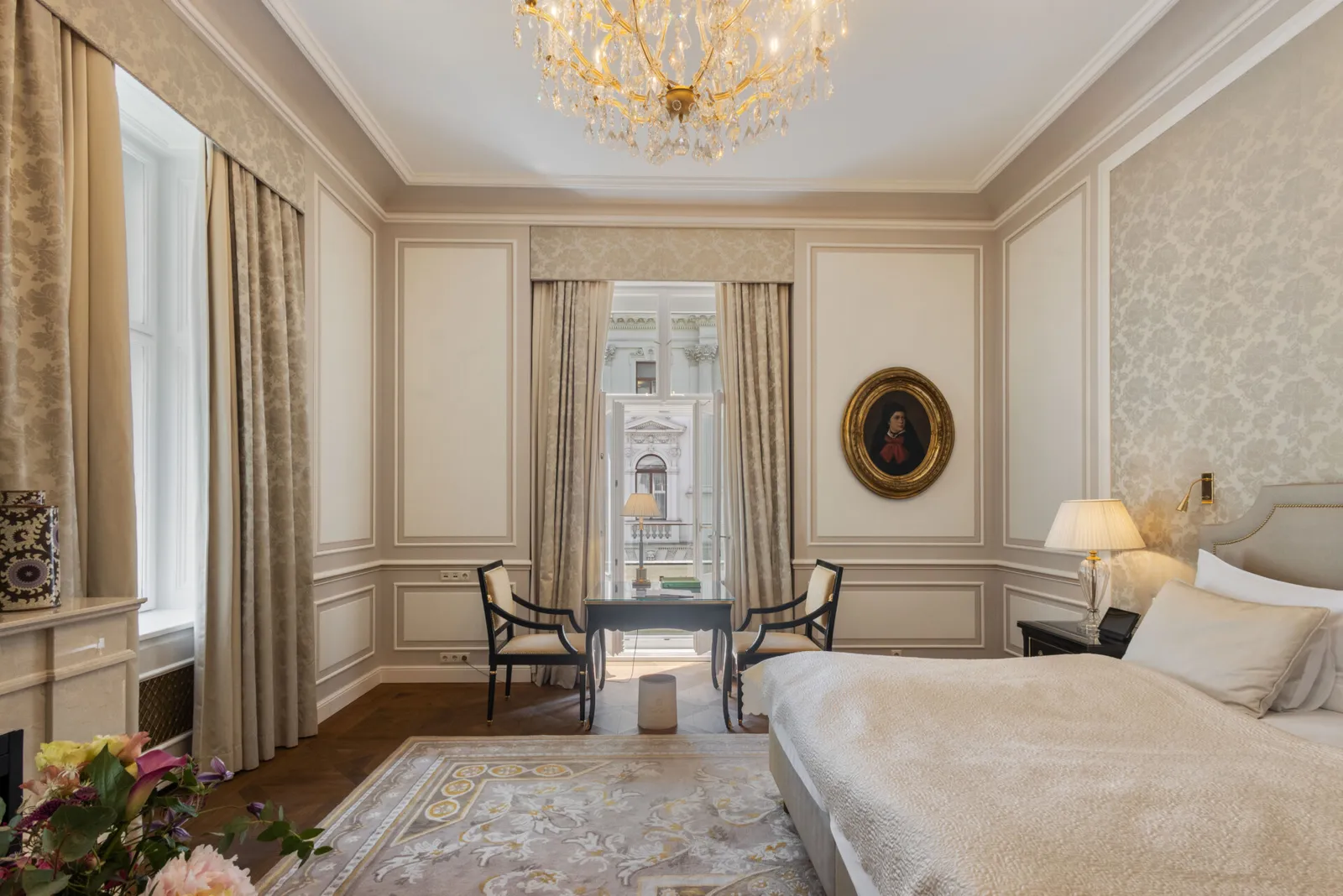A Junior Suite with view: the bed, a desk and 2 chairs at the window, gold curtains and a crystal chandelier.