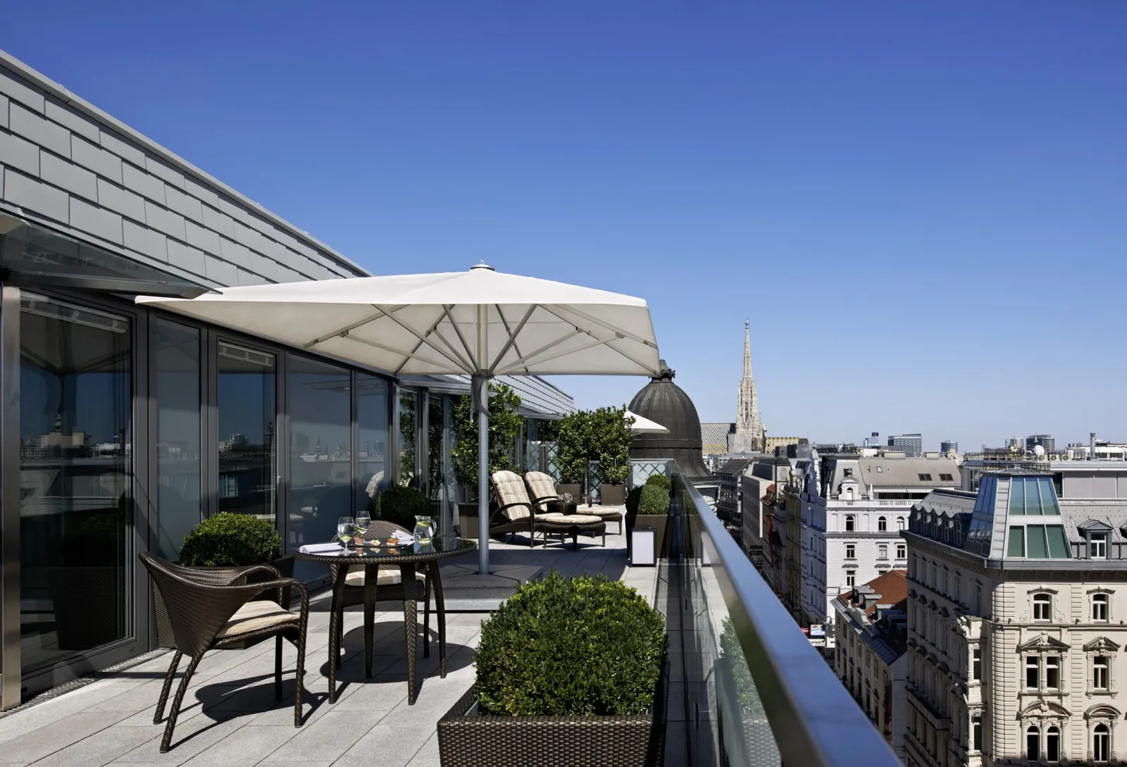 The Opera Penthouse Suite terrace: a table under a white parasol, potted hedges and, beyond the roofs, the spire of St Stephen’s.