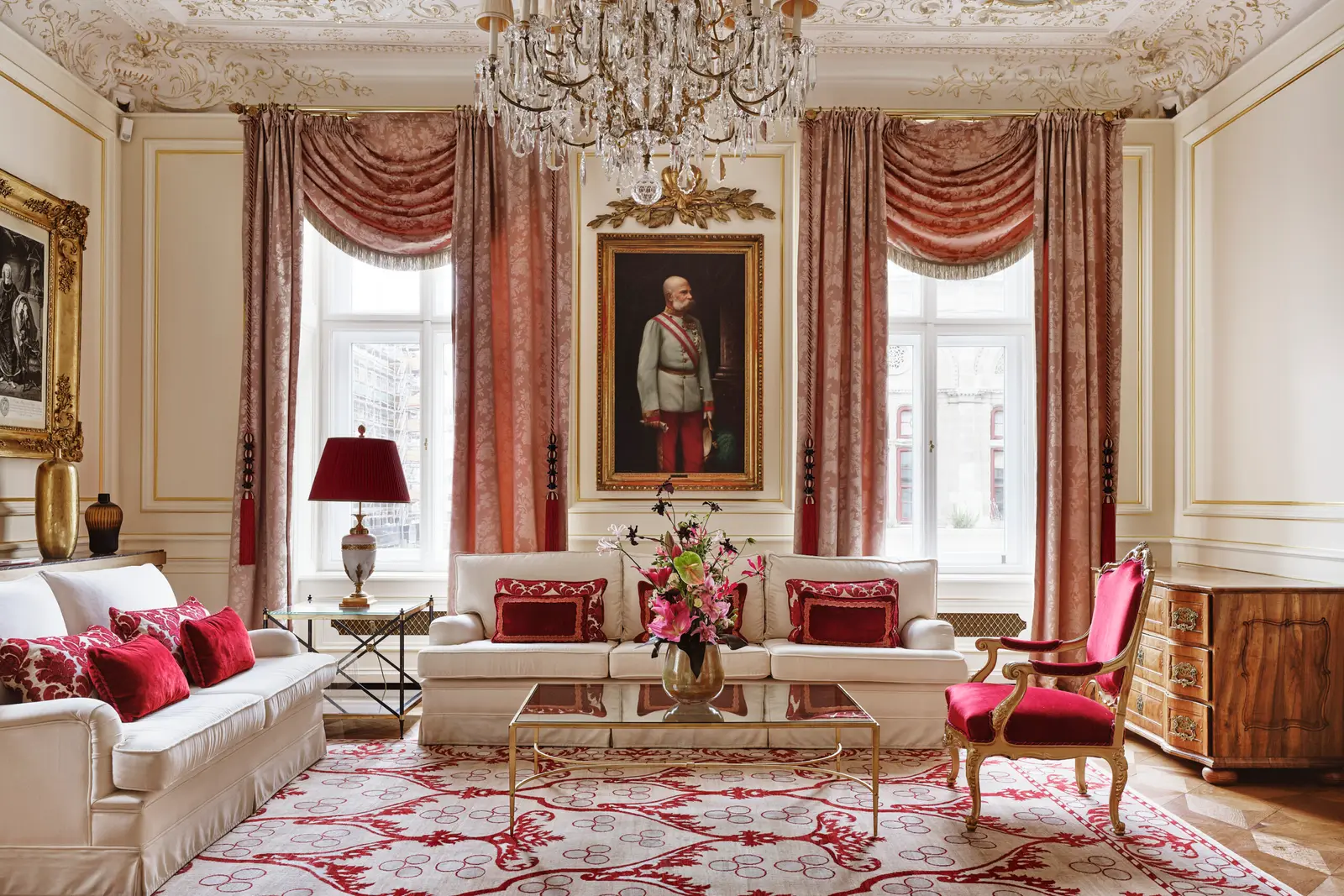 The Wiener Philharmoniker Suite sitting room: pale sofas with red cushions, swagged curtains, a stucco ceiling and the portrait of a man in uniform.