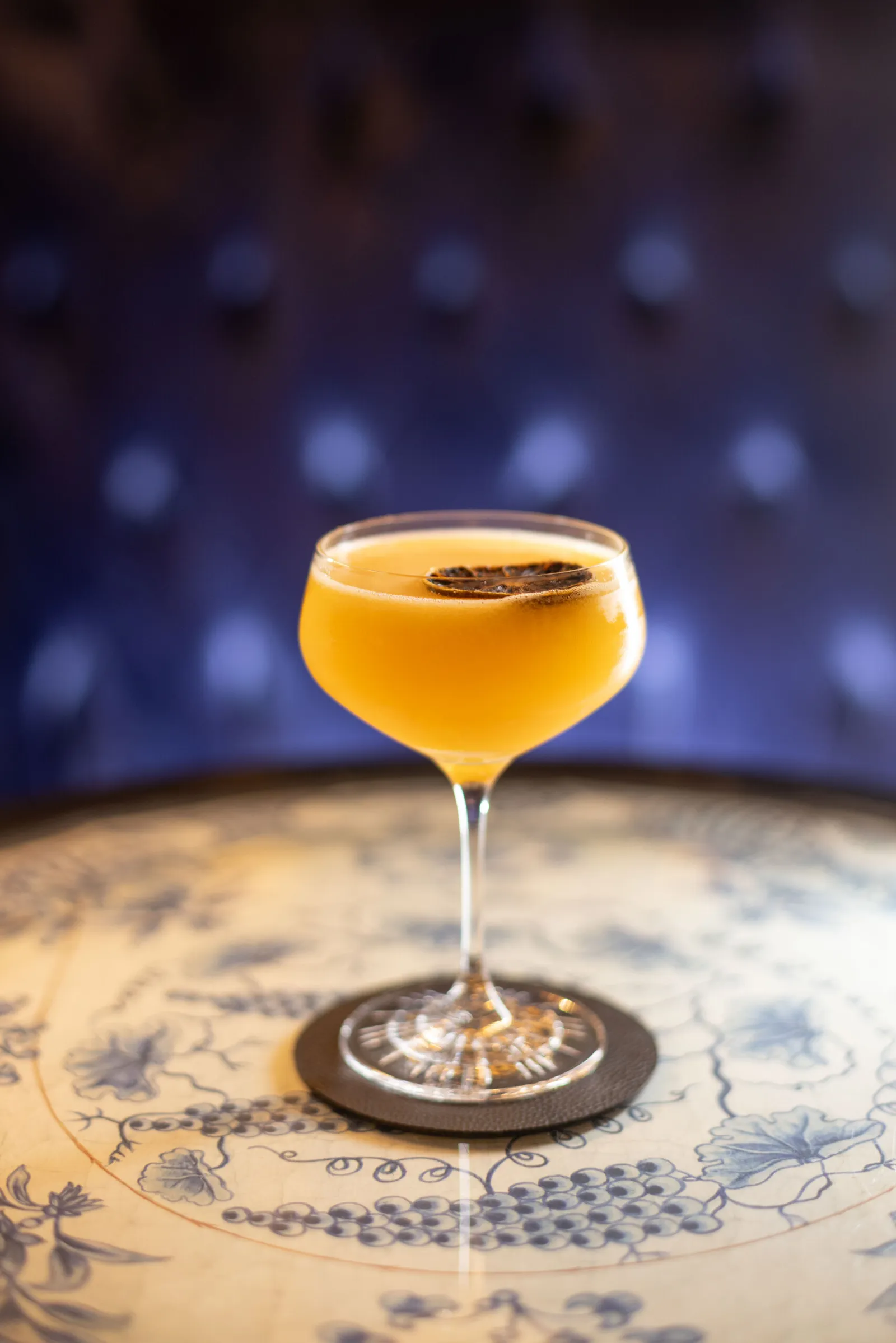 An apricot-coloured cocktail in a stemmed coupe on a blue-patterned ceramic table in the Blaue Bar.