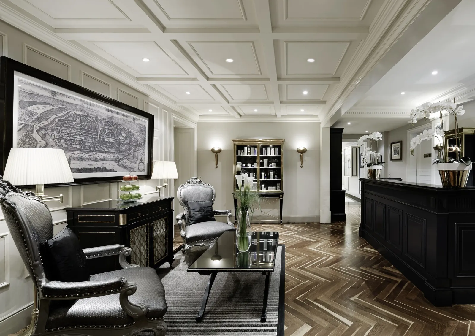 The Sacher Boutique Spa lounge: black armchairs, a large framed map on the wall, herringbone parquet and the reception desk.
