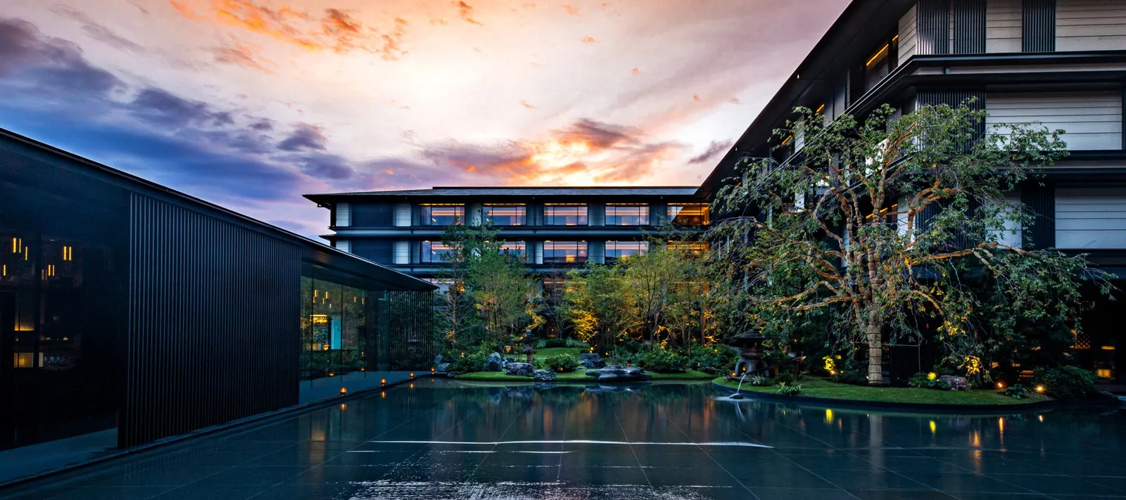 The inner garden at sunset: the dark sheet of water, the trees and the hotel’s low wings under a pink sky.