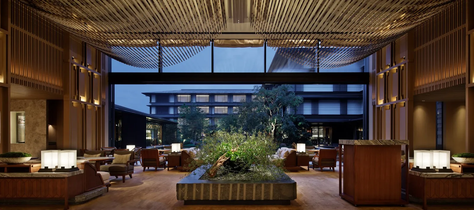 The lobby with its slatted timber ceiling, the low armchairs and the wide glass wall onto the garden and the hotel’s wing.