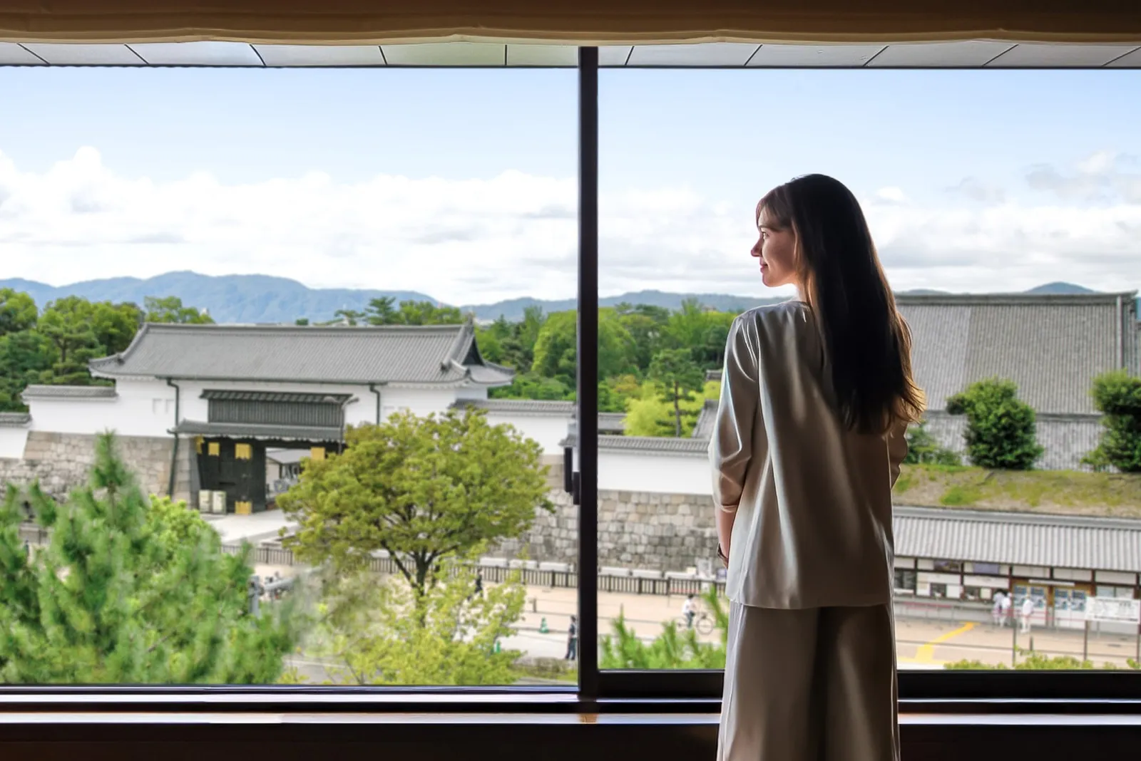 A guest at a room’s window looks out at Nijo-jo Castle: the walls, the Higashi Otemon Gate and Kyoto’s hills beyond.
