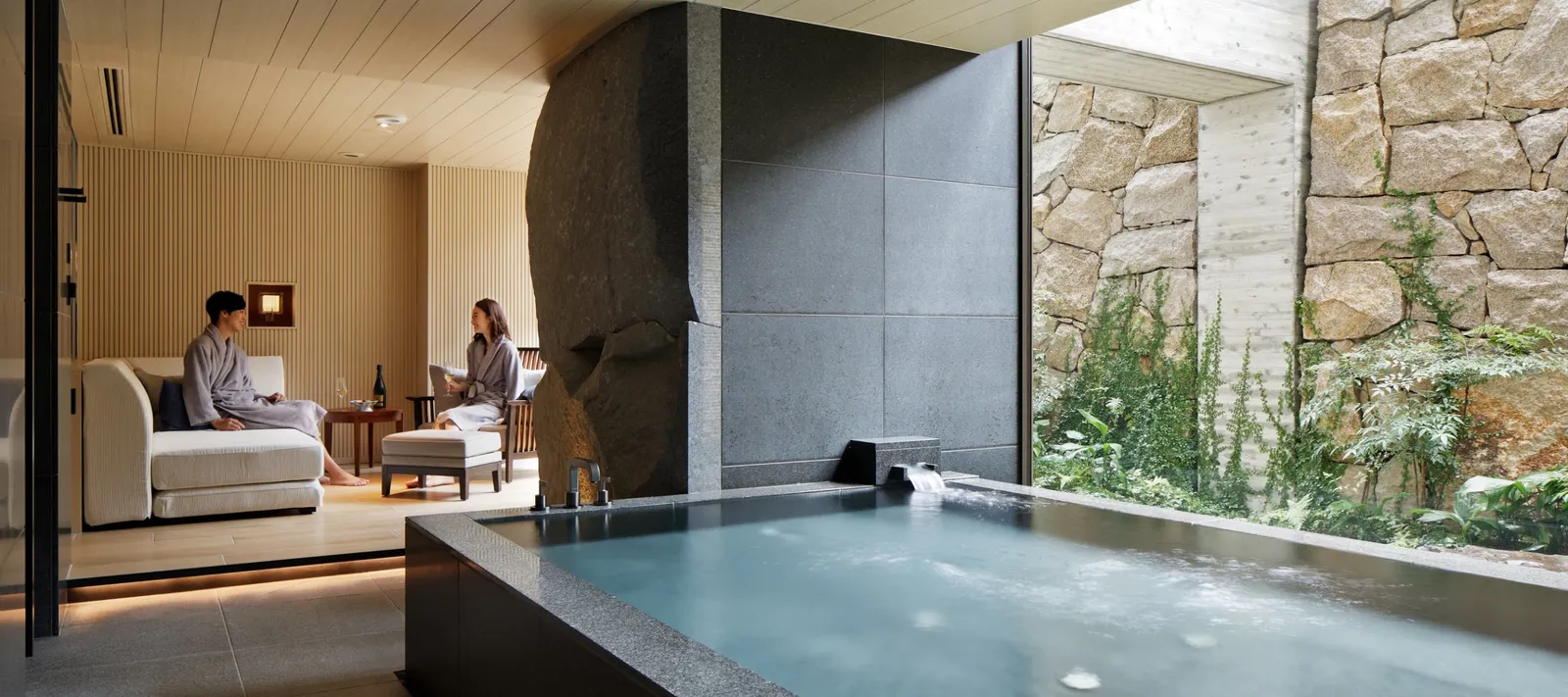 One of the 2 private onsen: the stone tub full of spring water, the lounge where a couple in robes rest and the planted stone wall.