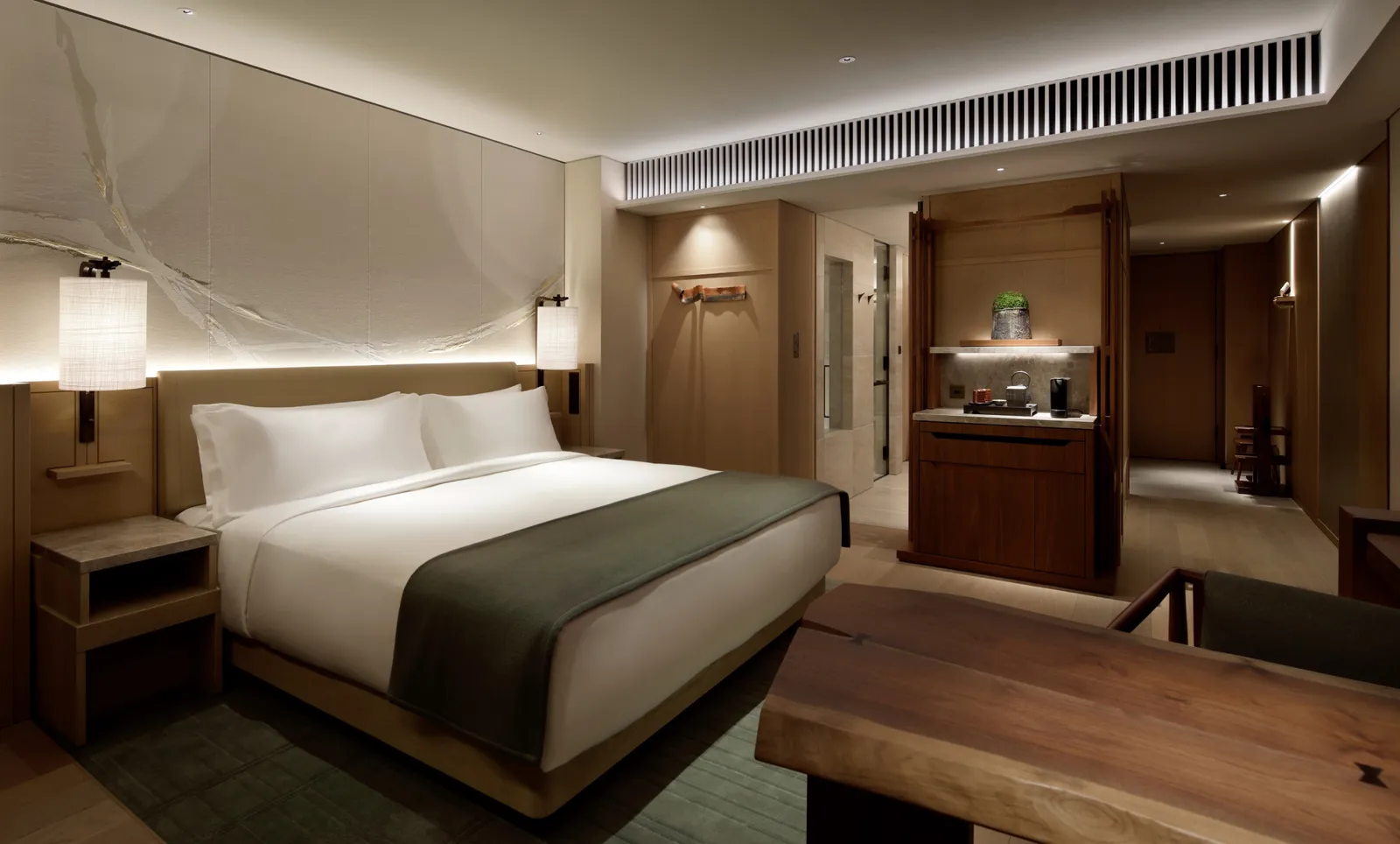 A Deluxe Room: the king bed with its green throw, the solid-wood table and the washi paper wall.