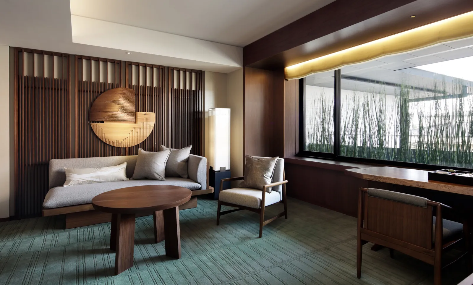 A Deluxe Suite’s living room: the low sofa, the round wooden table and the long window onto bamboo.