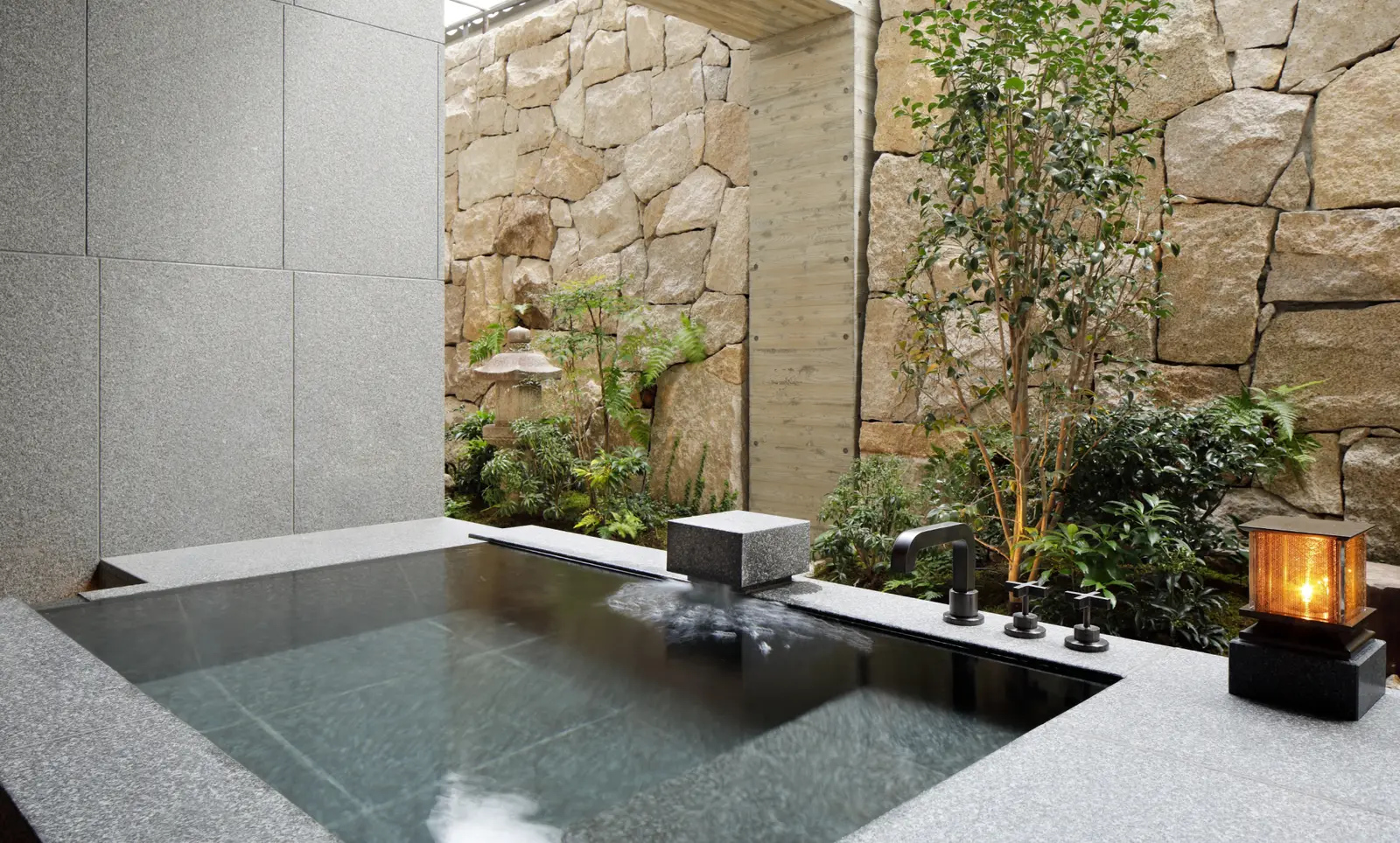 The Onsen Suite’s open-air bath: the stone tub full of spring water, the trees and the dry-stone wall.