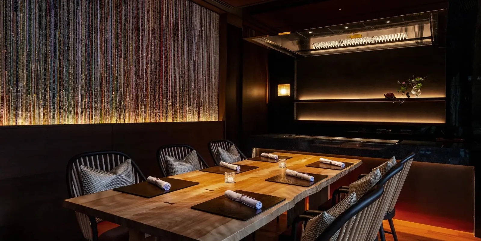 TOKI’s private dining room: a wooden table laid for 6 under low lights, with a lit bamboo wall behind.
