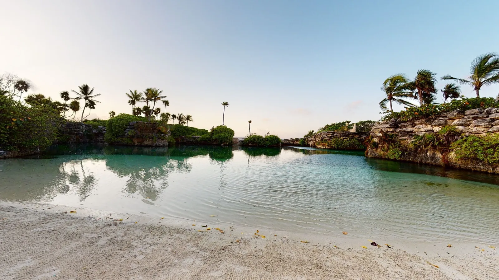 A cove in the resort: white sand, still water and rocks covered in green