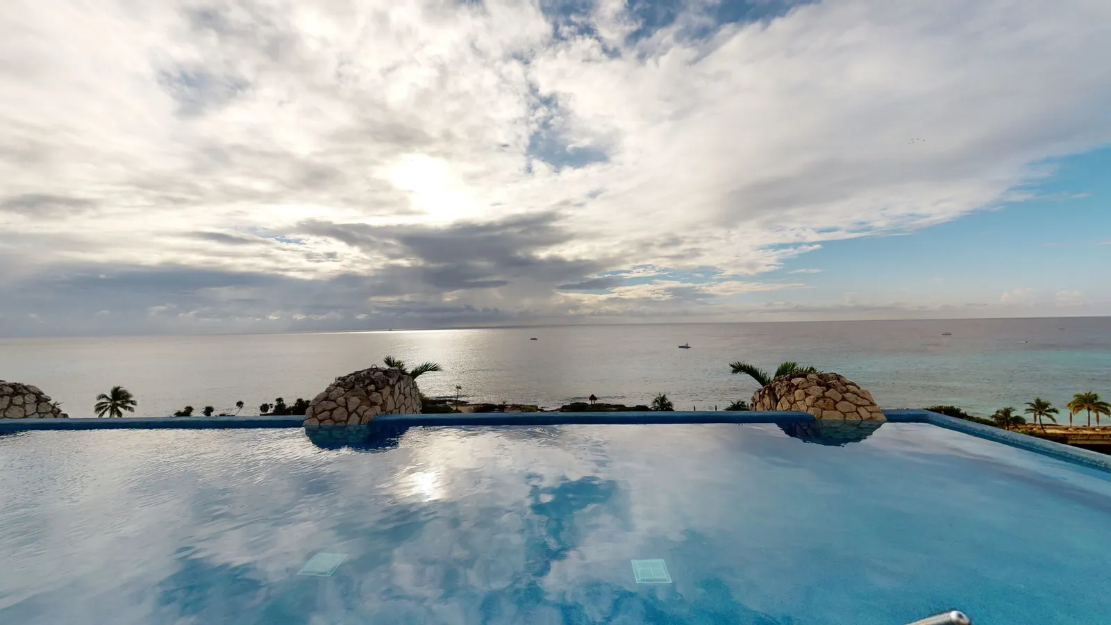 The edge of a rooftop pool reaching towards the Caribbean, between 2 large sculpted turtle shells