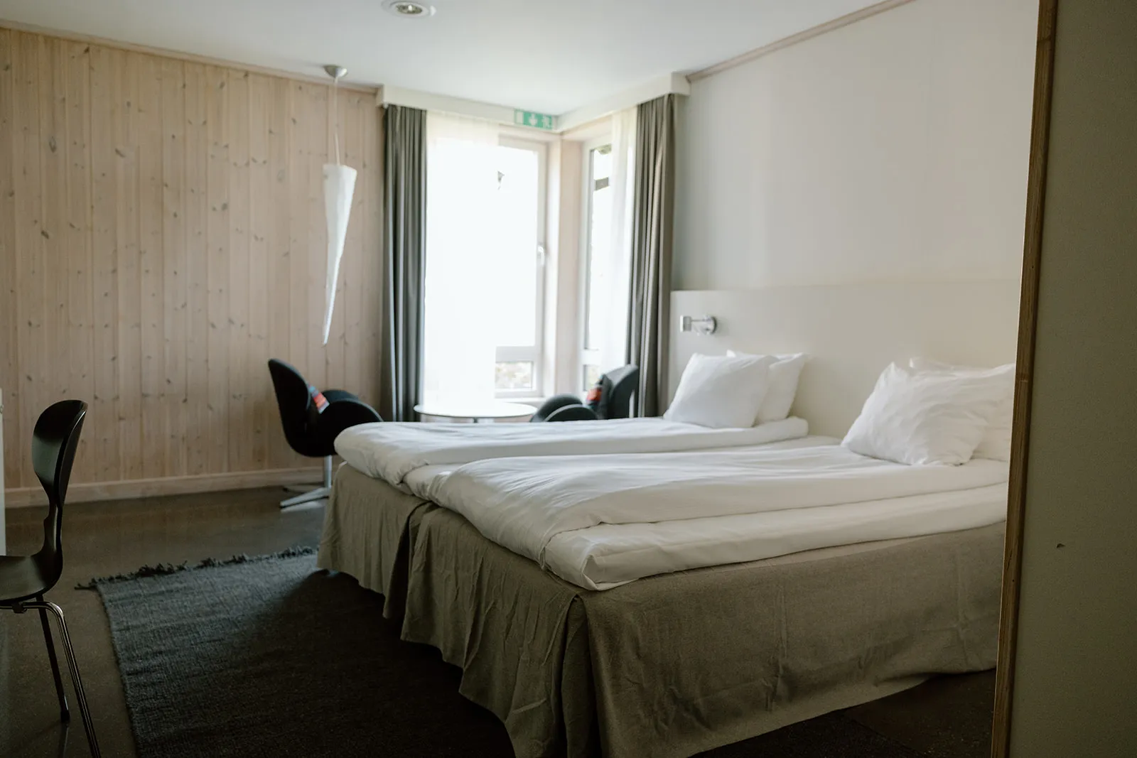 A Kaamos Superior room: 2 beds with white linen, pale timber walls, a dark rug, armchairs and a round table by the window.