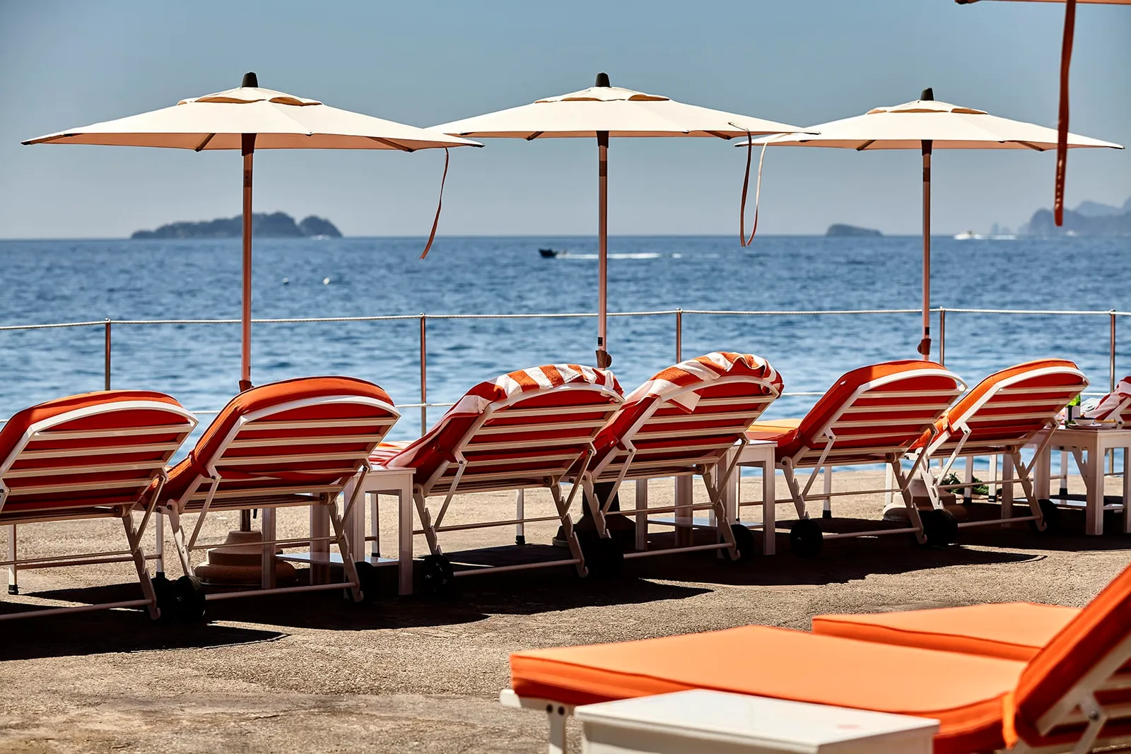 Orange-striped loungers under 3 pale parasols, facing the sea and the Li Galli islets.
