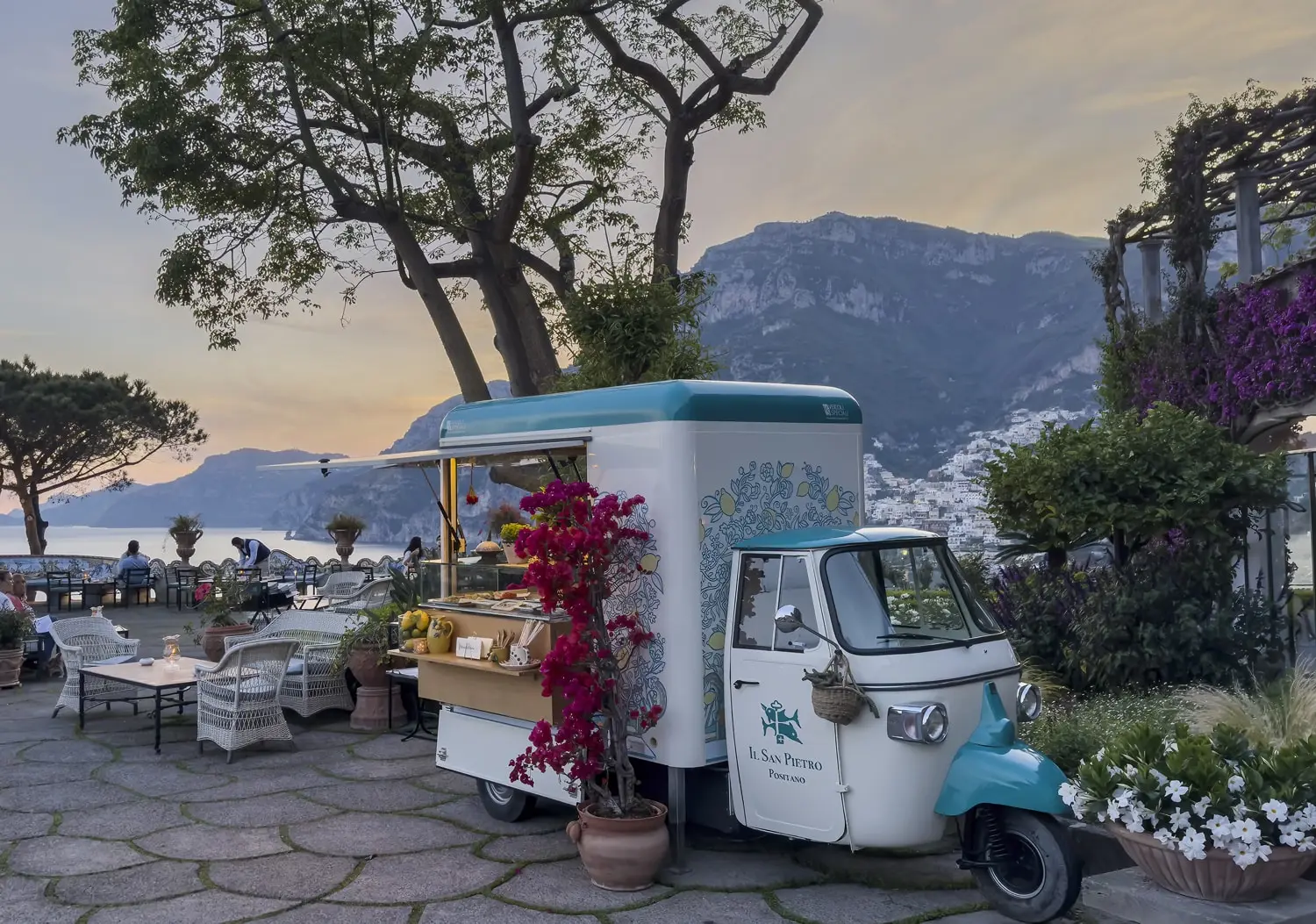 The 3-wheeled Ape of Bits & Bites on the terrace at sunset, with Positano on the coast behind.