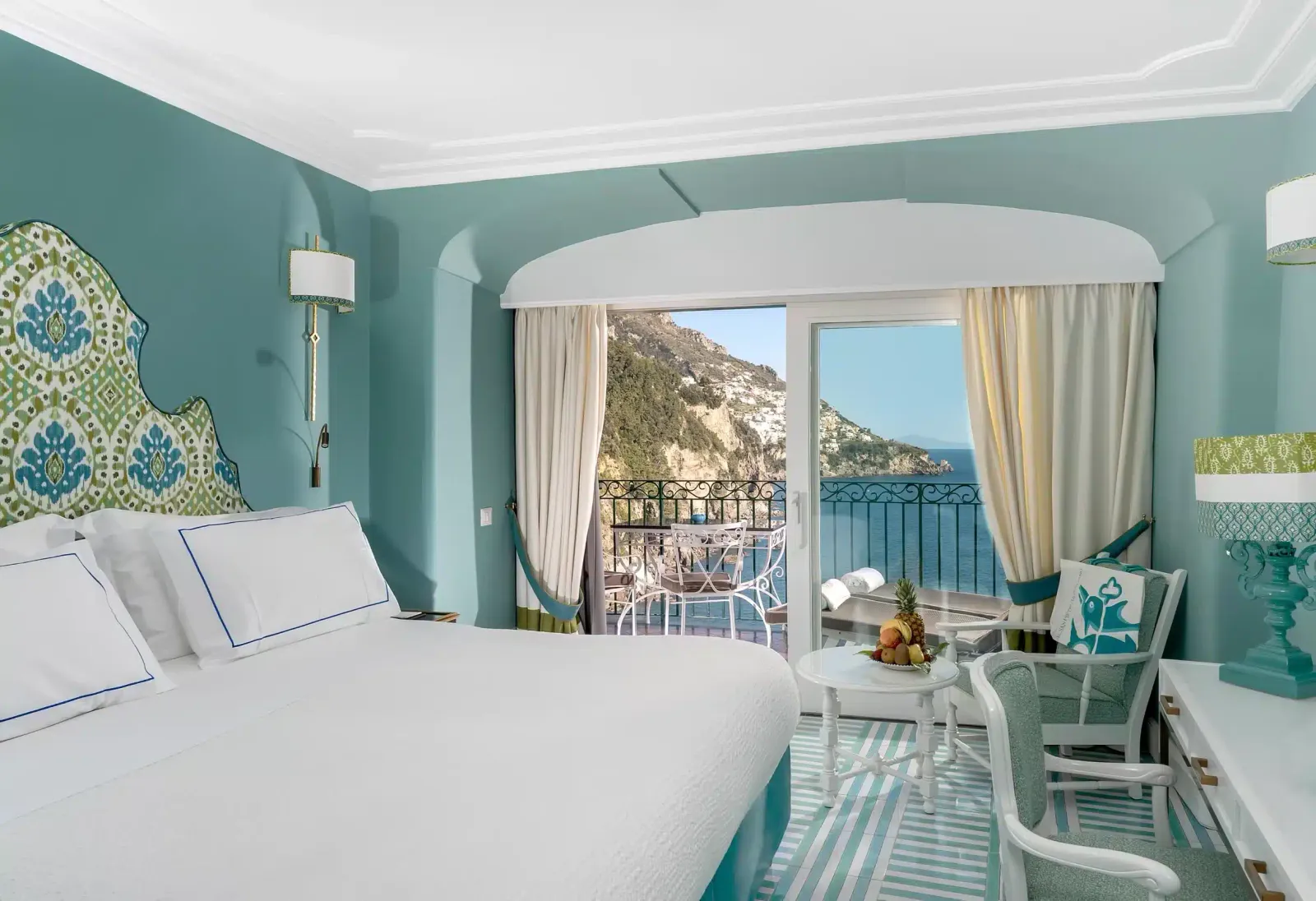 A Classic room with sea-green walls, the white bed and the French window open onto the terrace and the coast.