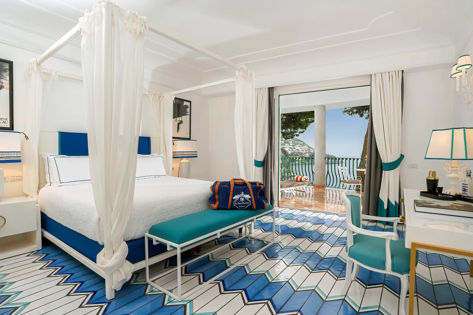 A Deluxe room with a white four-poster bed, a blue zigzag majolica floor and the terrace over the sea.