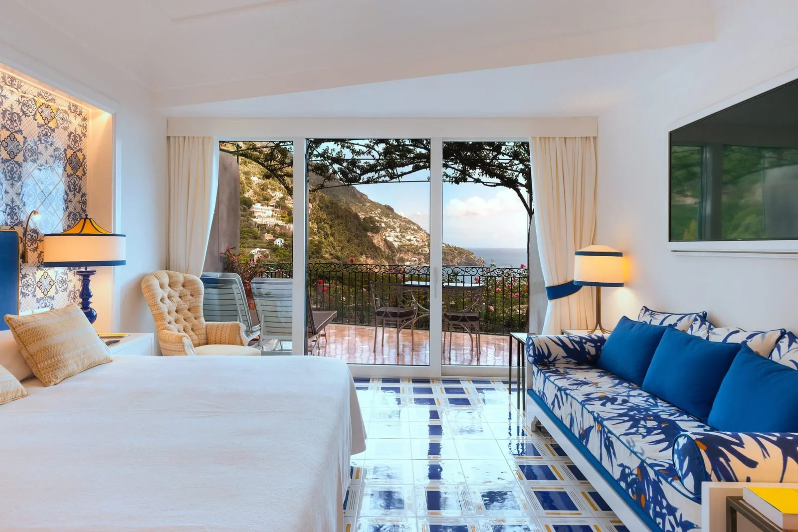 An Elite room with a blue floral sofa, a glossy ceramic floor and the windows onto the terrace towards Positano.