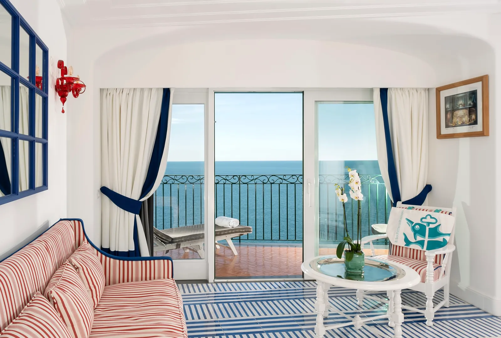 The sitting area of a Signature room, with a red-striped sofa, a blue-striped floor and French windows onto the sea.