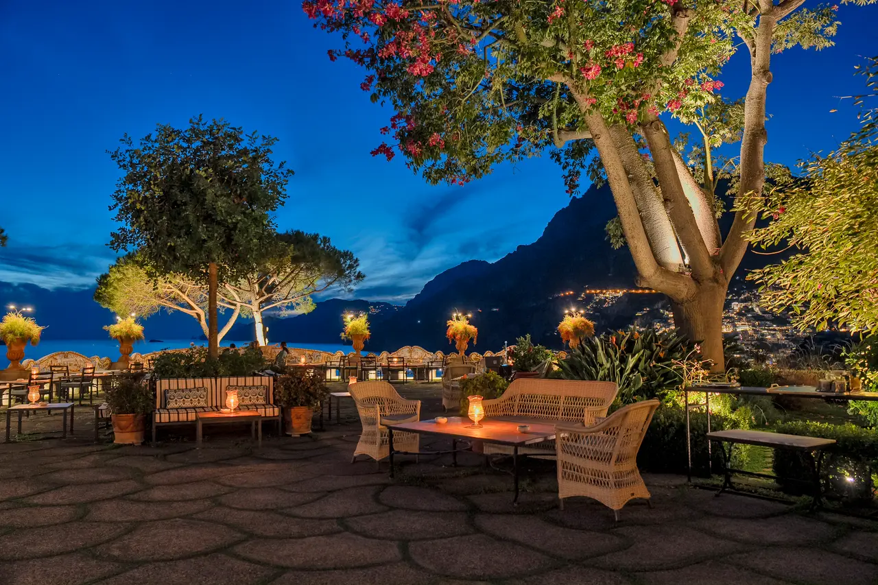 The great terrace at nightfall, with wicker armchairs, lit candles and the lights of Positano along the coast.
