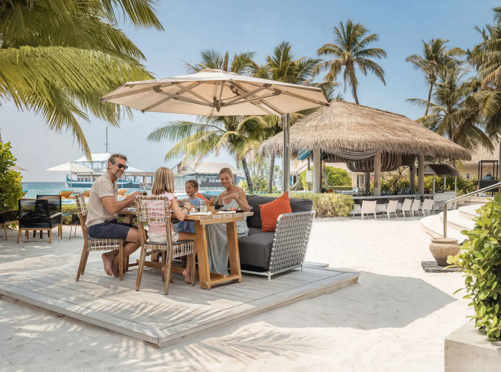 A family at breakfast on the sand outside Café Umi, under a parasol and the palms.