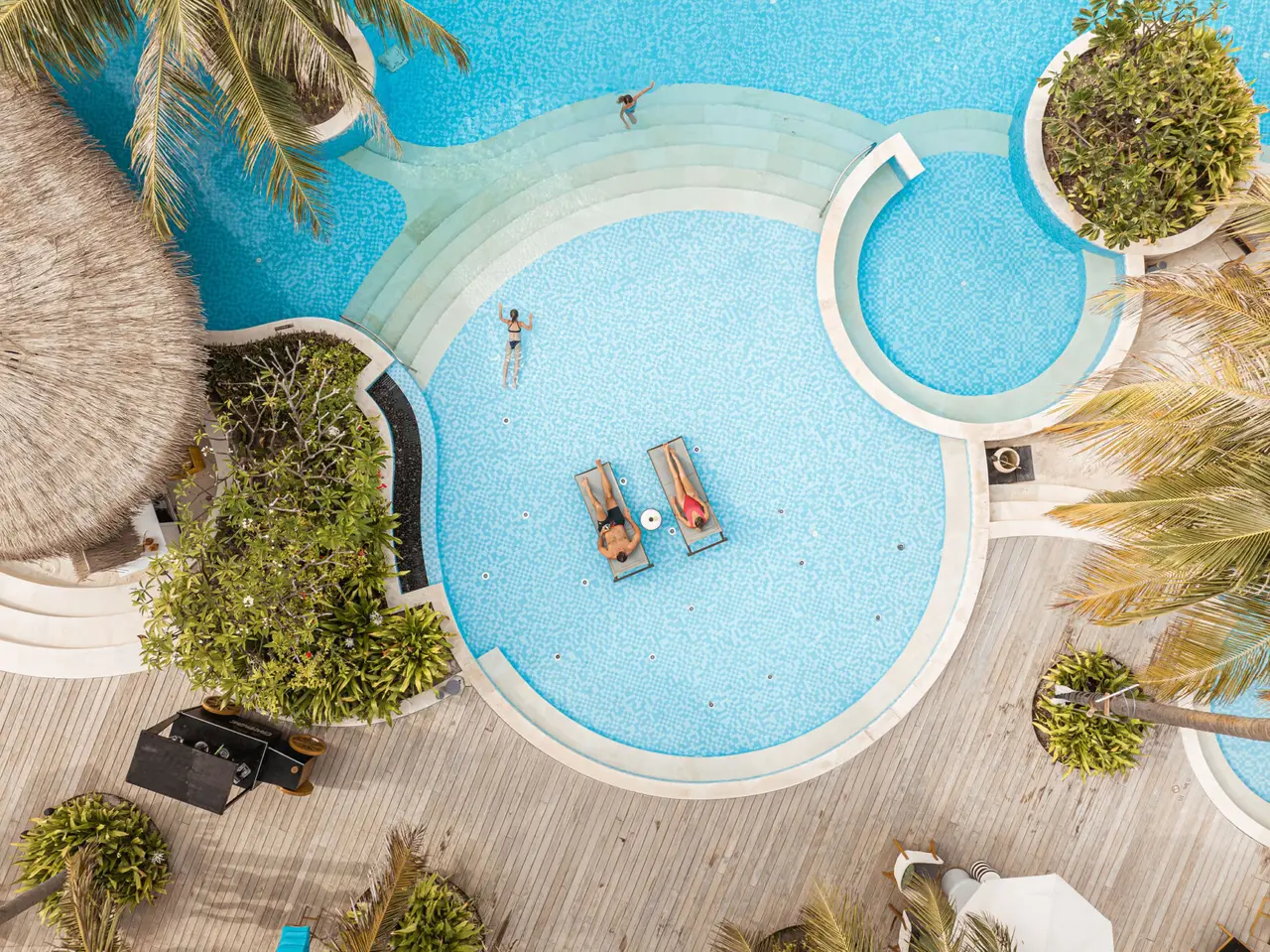 The main pool from above, round, with 2 loungers in the water and the deck around it.