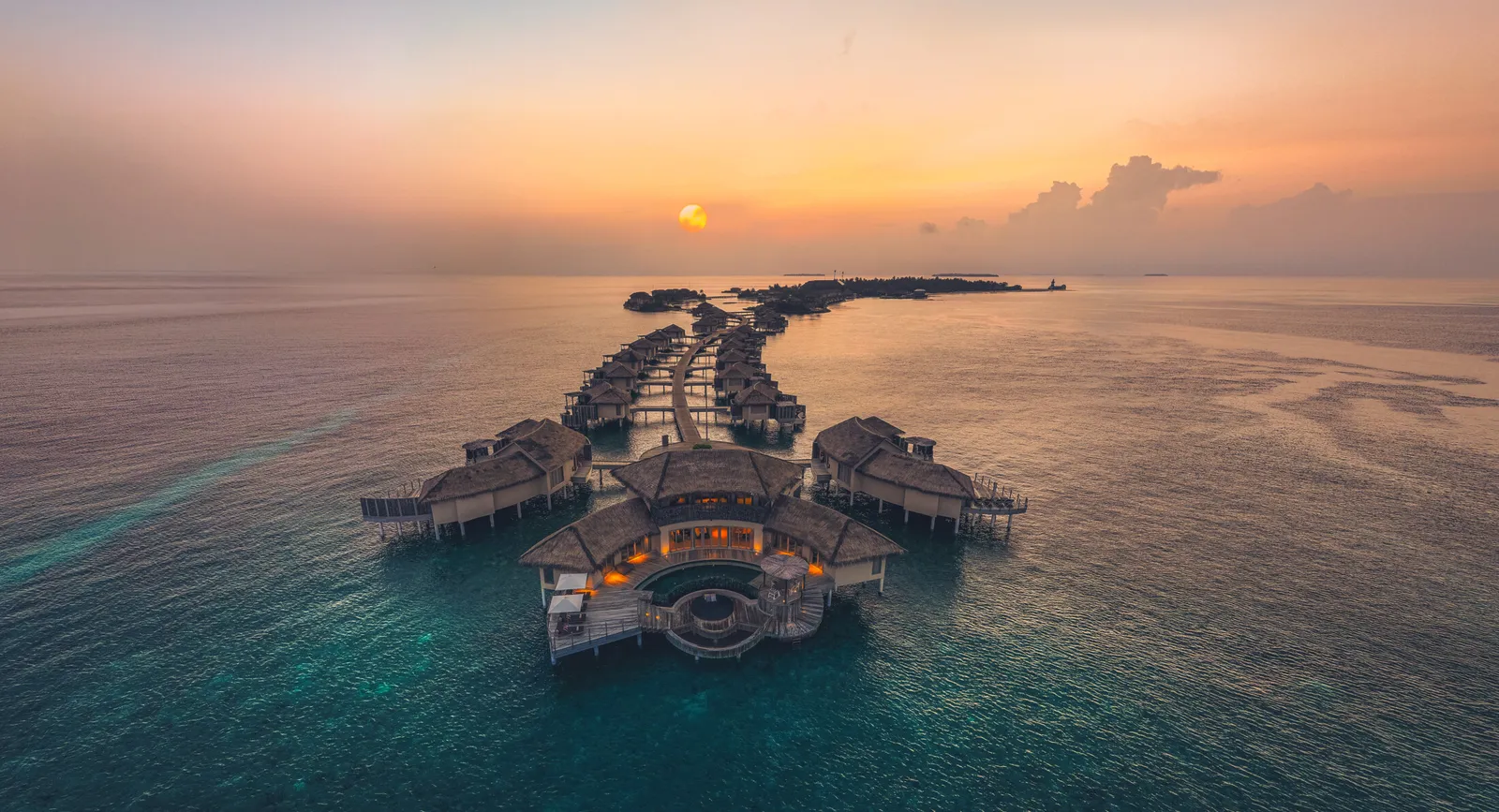 The water villas from above at dusk, in a line over the calm sea.