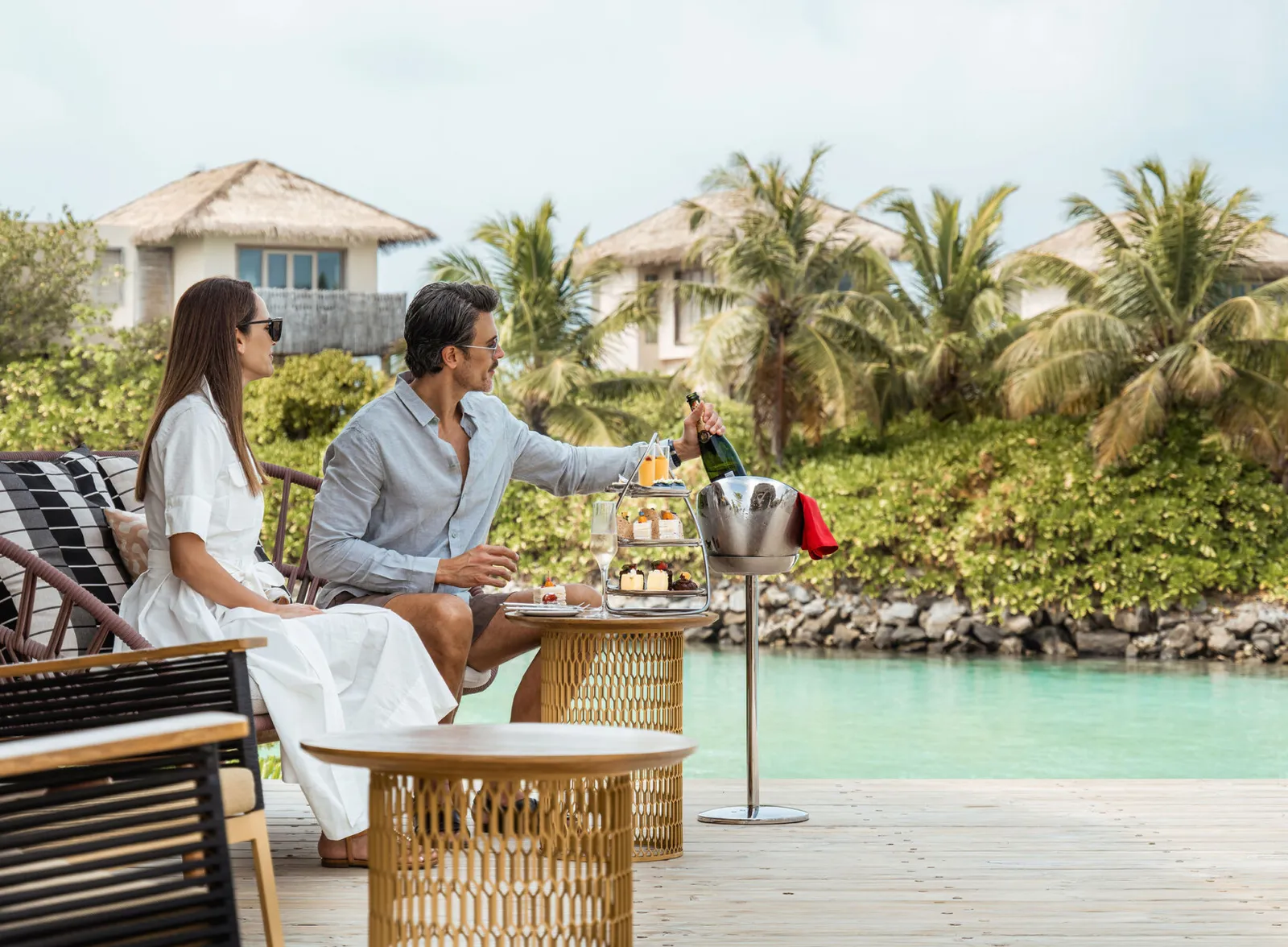 Afternoon tea at The Retreat: a couple with the cake stand and champagne beside the lagoon.