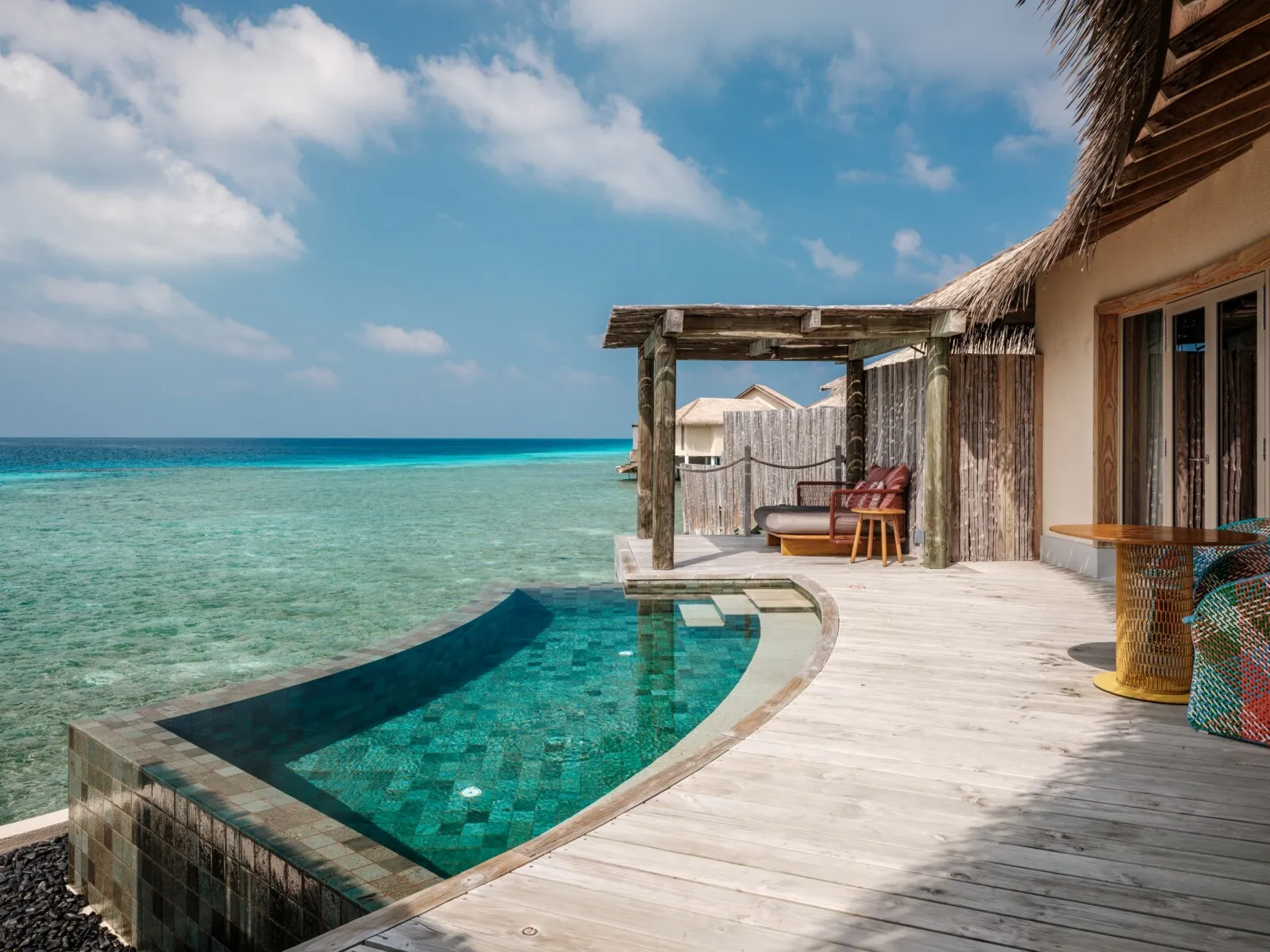 An Overwater Pool Villa’s deck: the curved infinity pool, the pergola and the ocean.