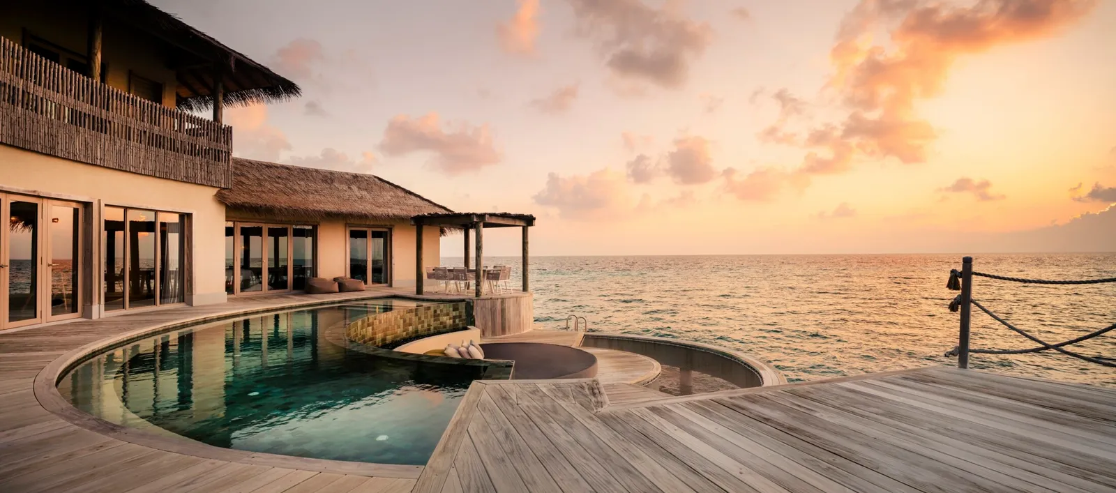 The Three Bedroom Overwater Pool Residence at sunset, the curved pool and the timber deck over the sea.