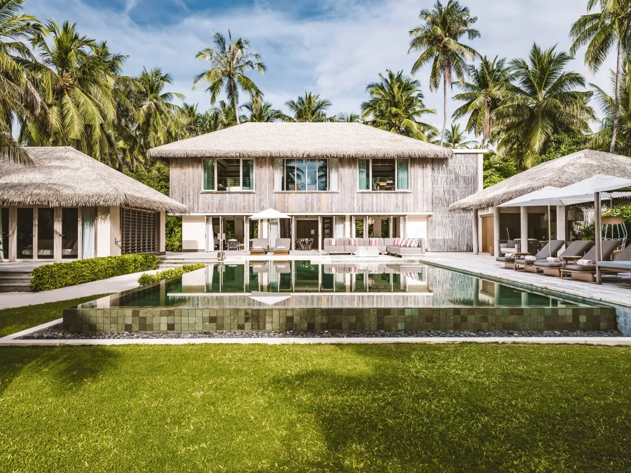The Three Bedroom Royal Beachfront Pool Residence, the 2-storey house with its pool and lawn among the palms.