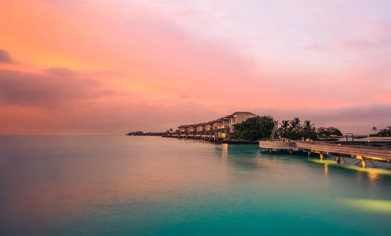 The 2-storey lagoon villas at sunset, lined up over the water beside the jetty.