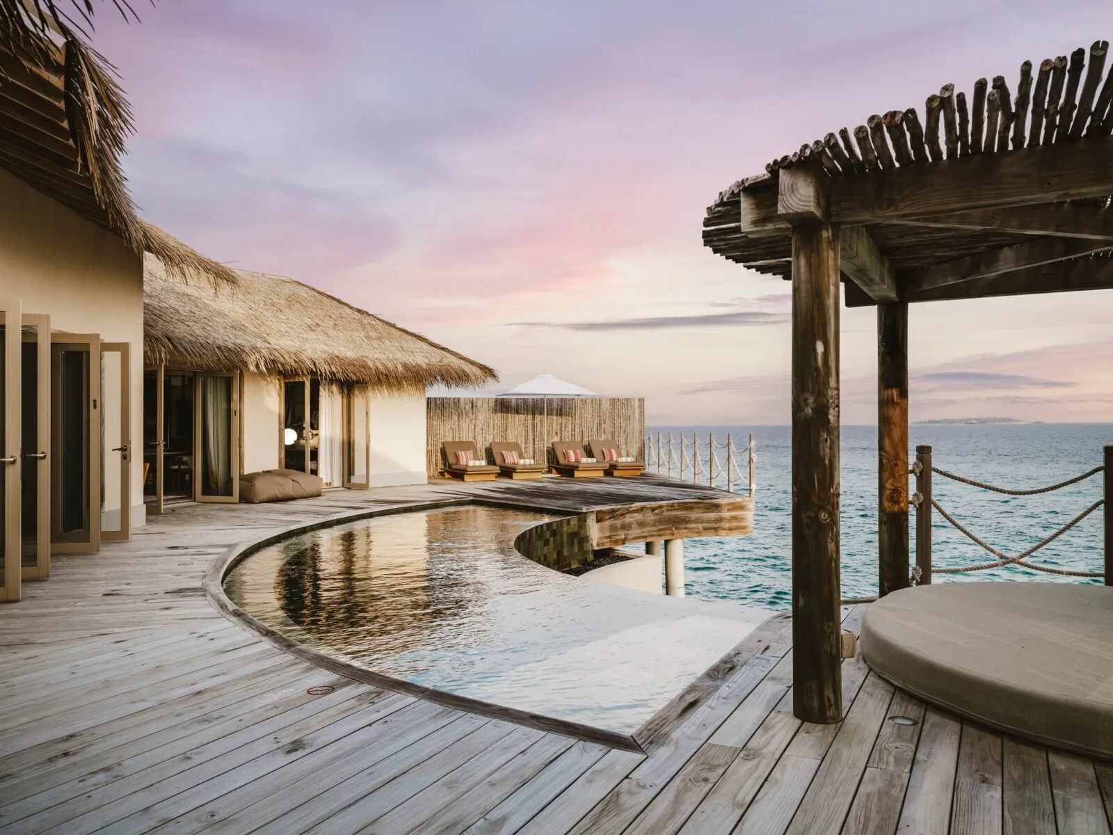 The Two Bedroom Overwater Pool Residence’s deck: the curved pool, the pergola and the sea at sunset.