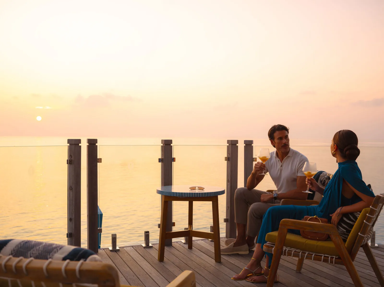 A couple on the Sunset Bar’s deck at sunset, with 2 cocktails.