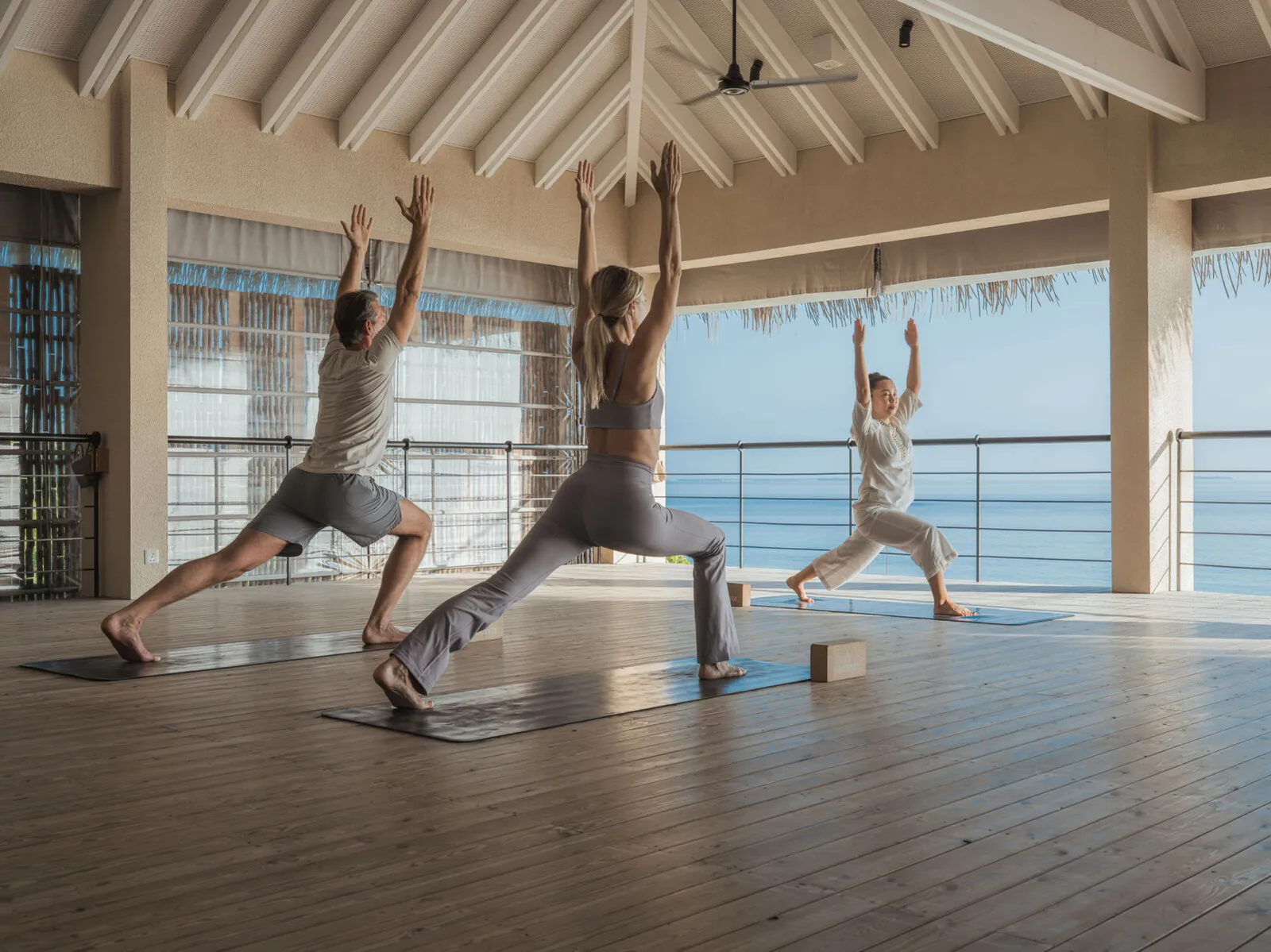 3 people in warrior pose in the yoga pavilion open to the sea.