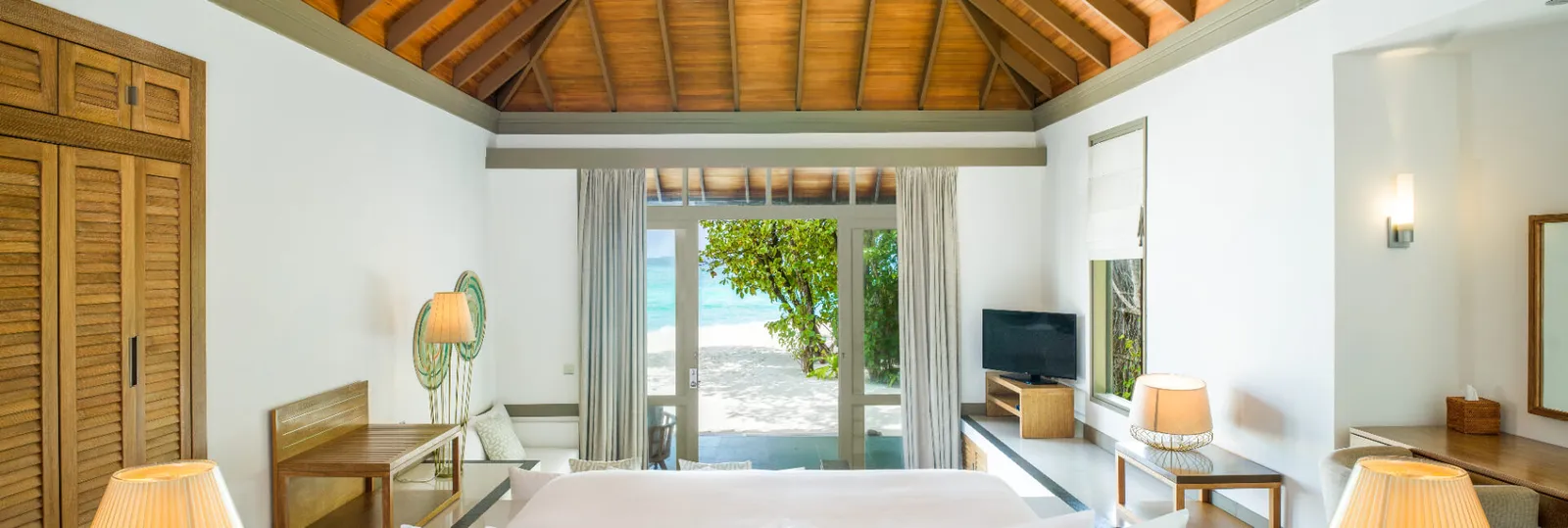 The Beach Villa lounge opening towards the deck and sea through trees.