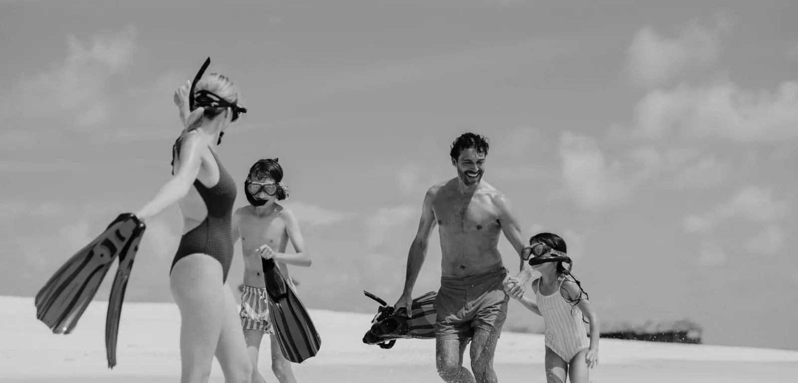 A family with masks and fins on the beach in an official black-and-white photograph.