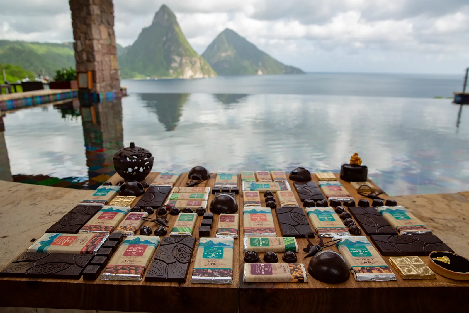 The estate’s chocolate bars and pieces laid out on a timber table, in front of the Jade Mountain Club’s pool and the Pitons under cloud.