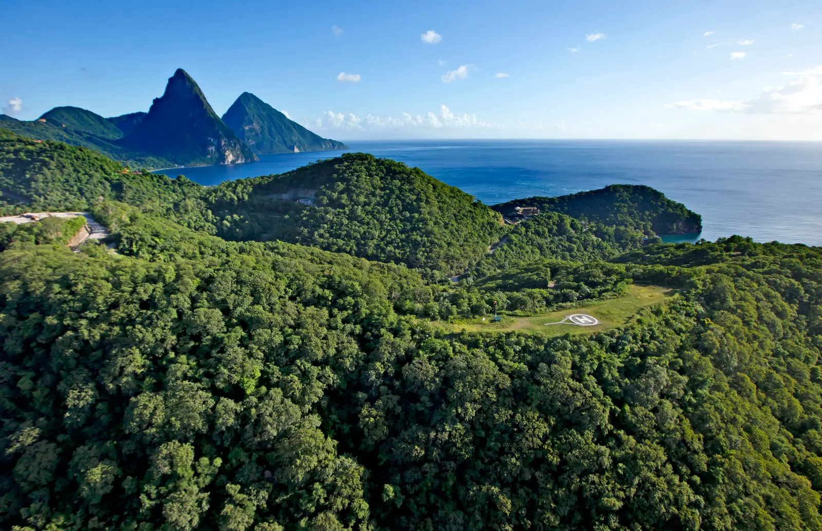 The Soufrière coast from the air: forest, the helipad in a clearing on the hill, the sea and the Pitons in the distance.