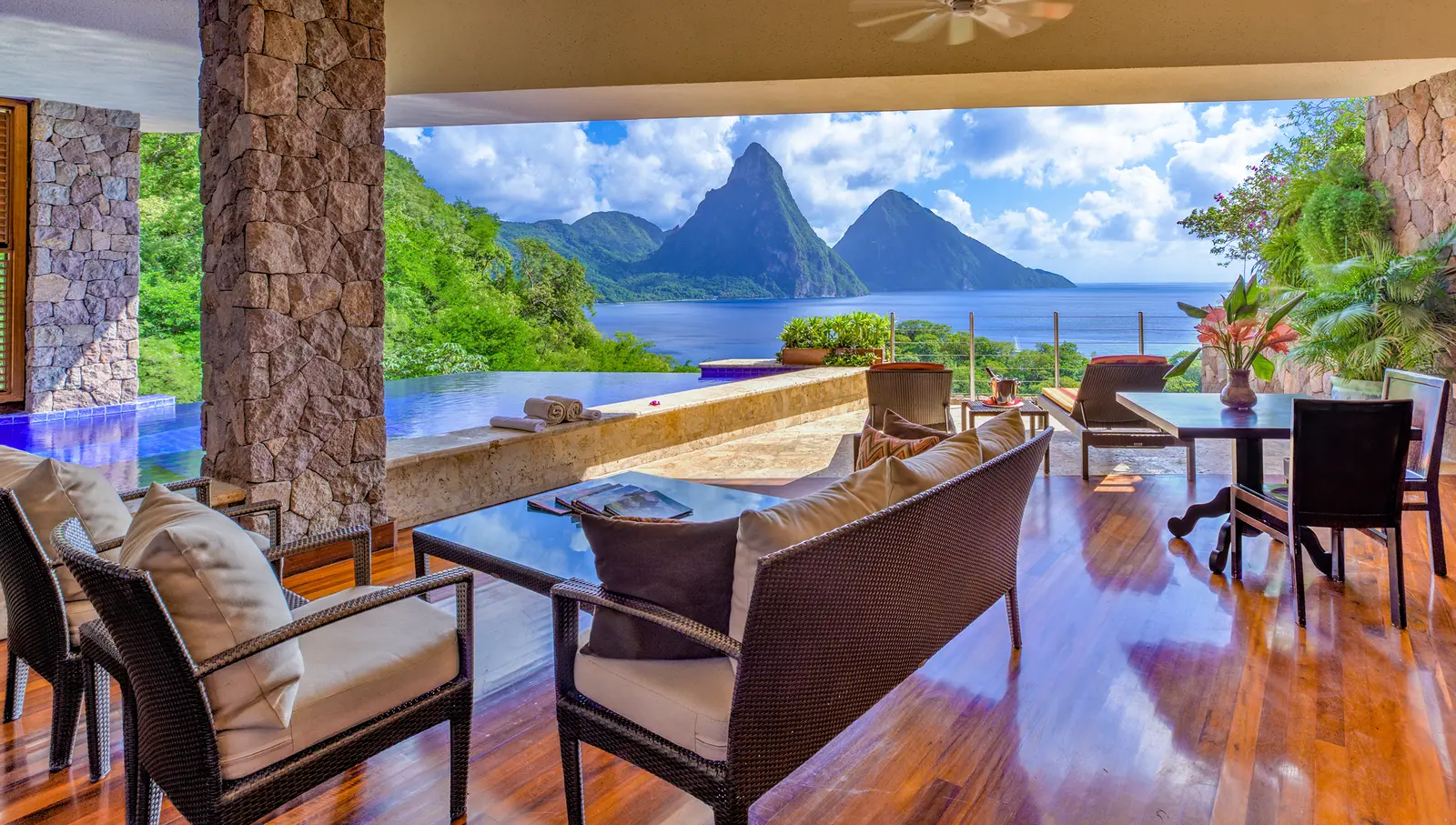 Inside a sanctuary open to the landscape: wicker sofas on a polished timber floor, stone pillars, the infinity pool and the Pitons where a fourth wall would be.