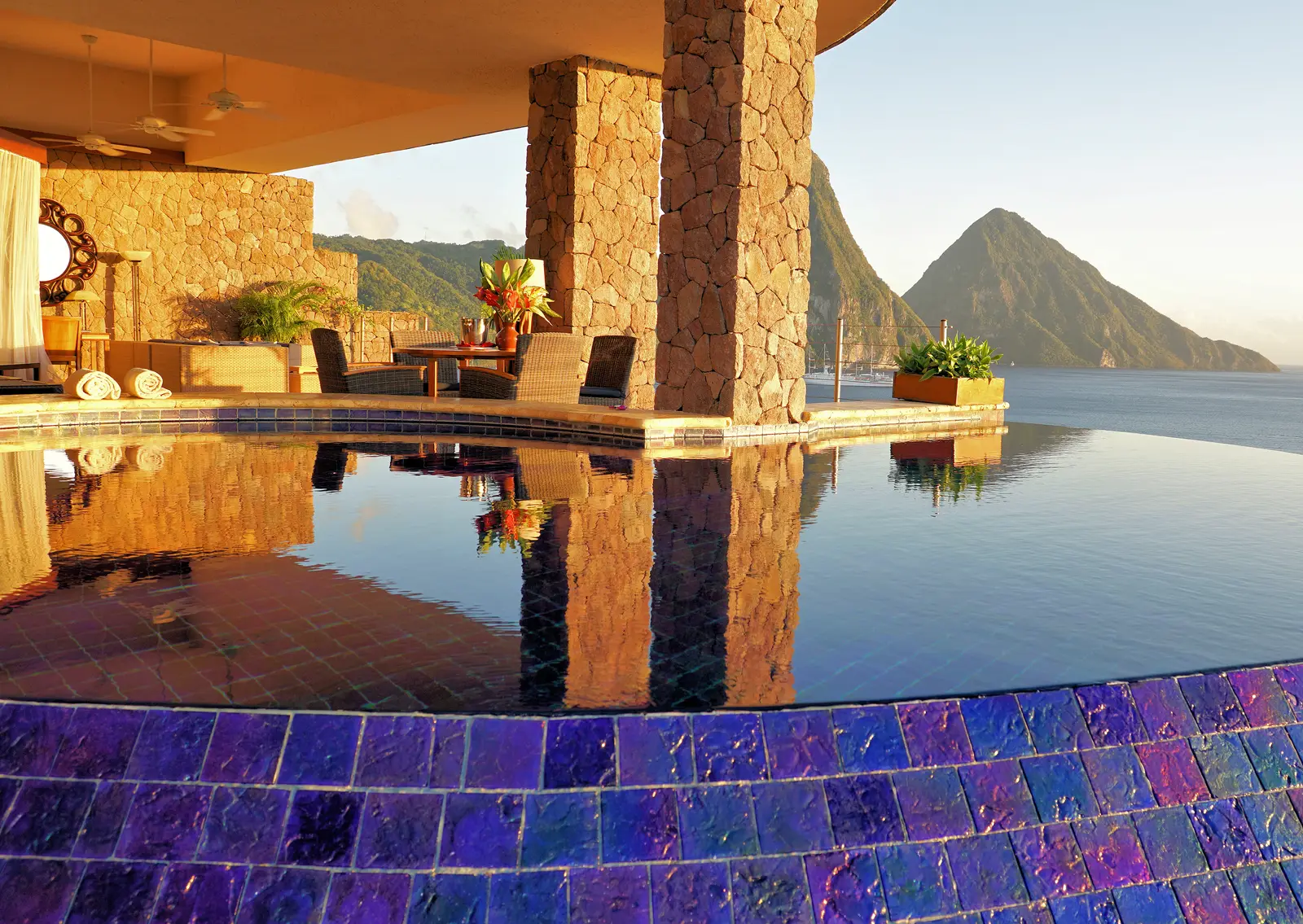 A Galaxy sanctuary: the infinity pool lined with violet tiles, the living area between stone pillars and Petit Piton in late-afternoon light.
