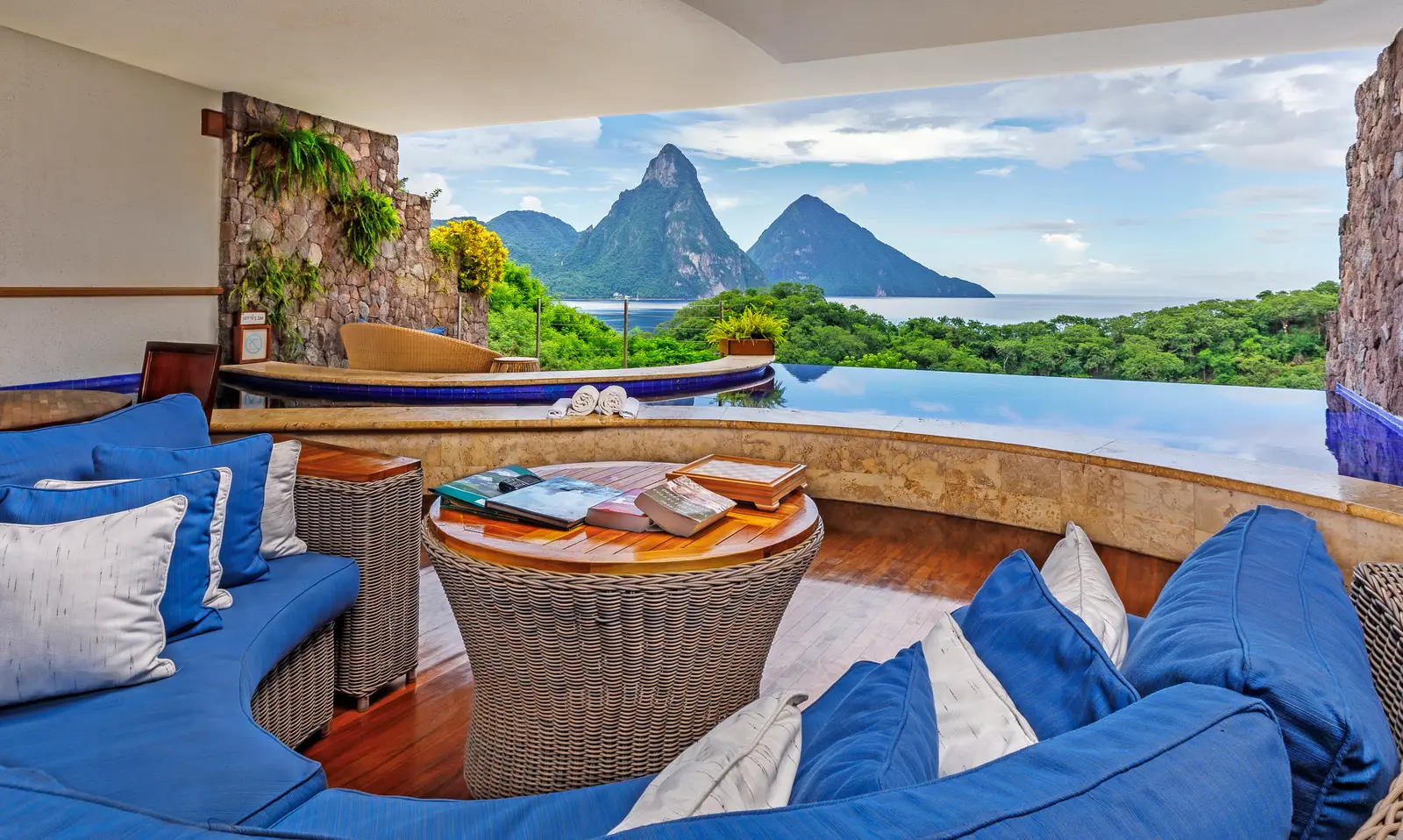 A Moon sanctuary: a curved blue sofa round a wicker table, the infinity pool beyond its stone rim and the Pitons ahead, with no glass between.