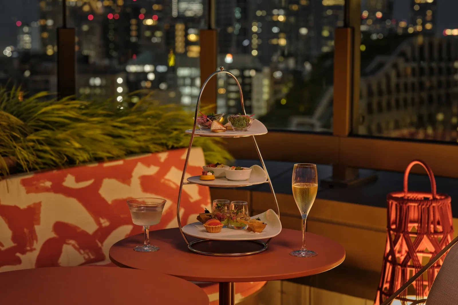 The evening high tea stand on the Garden Terrace, with 2 glasses and a lantern, and Tokyo lit up behind.