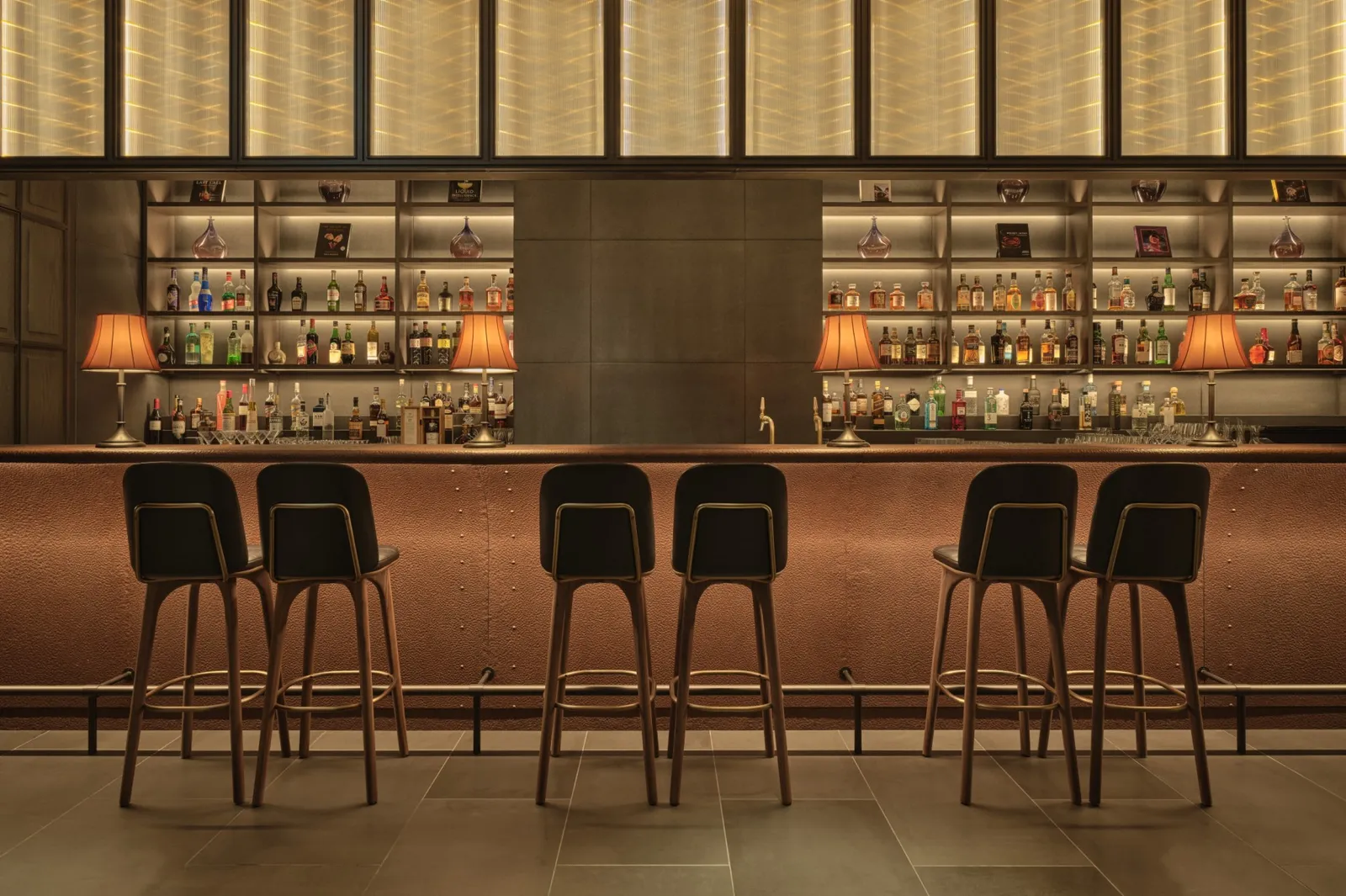 The Grill Bar counter, with 6 stools, lamps and bottles lit on the shelves.