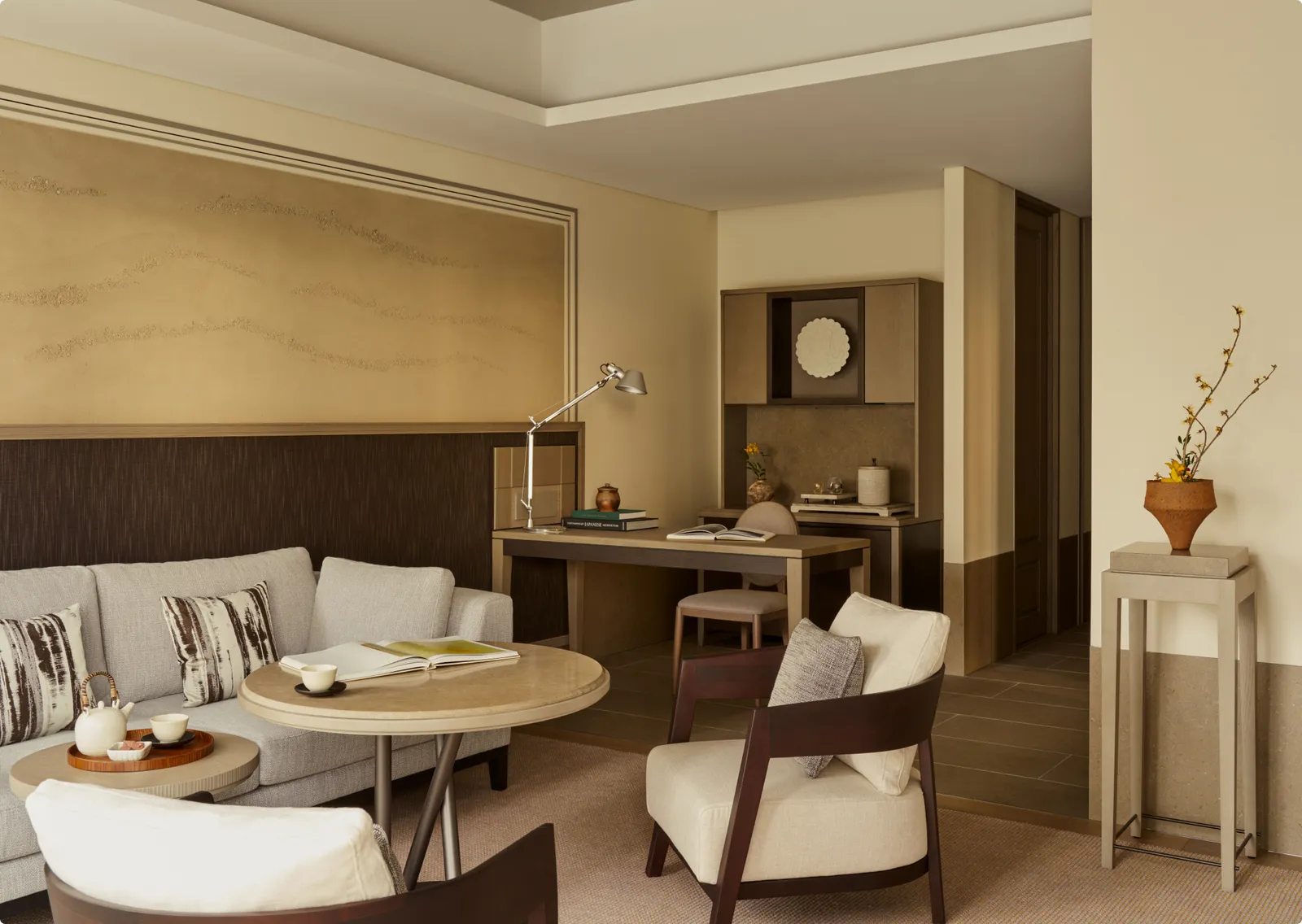 A Junior Suite living room: sofa, round table, writing desk and a flowering branch in a vase.