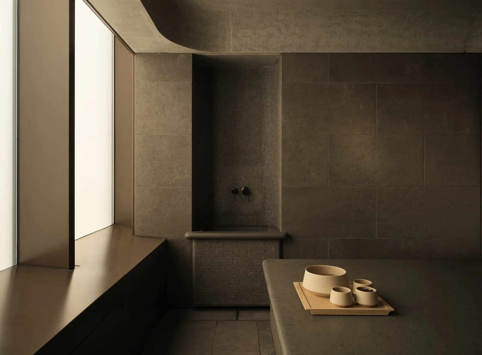 A Spa House hammam: dark stone walls, the marble bench and a tray of bowls.