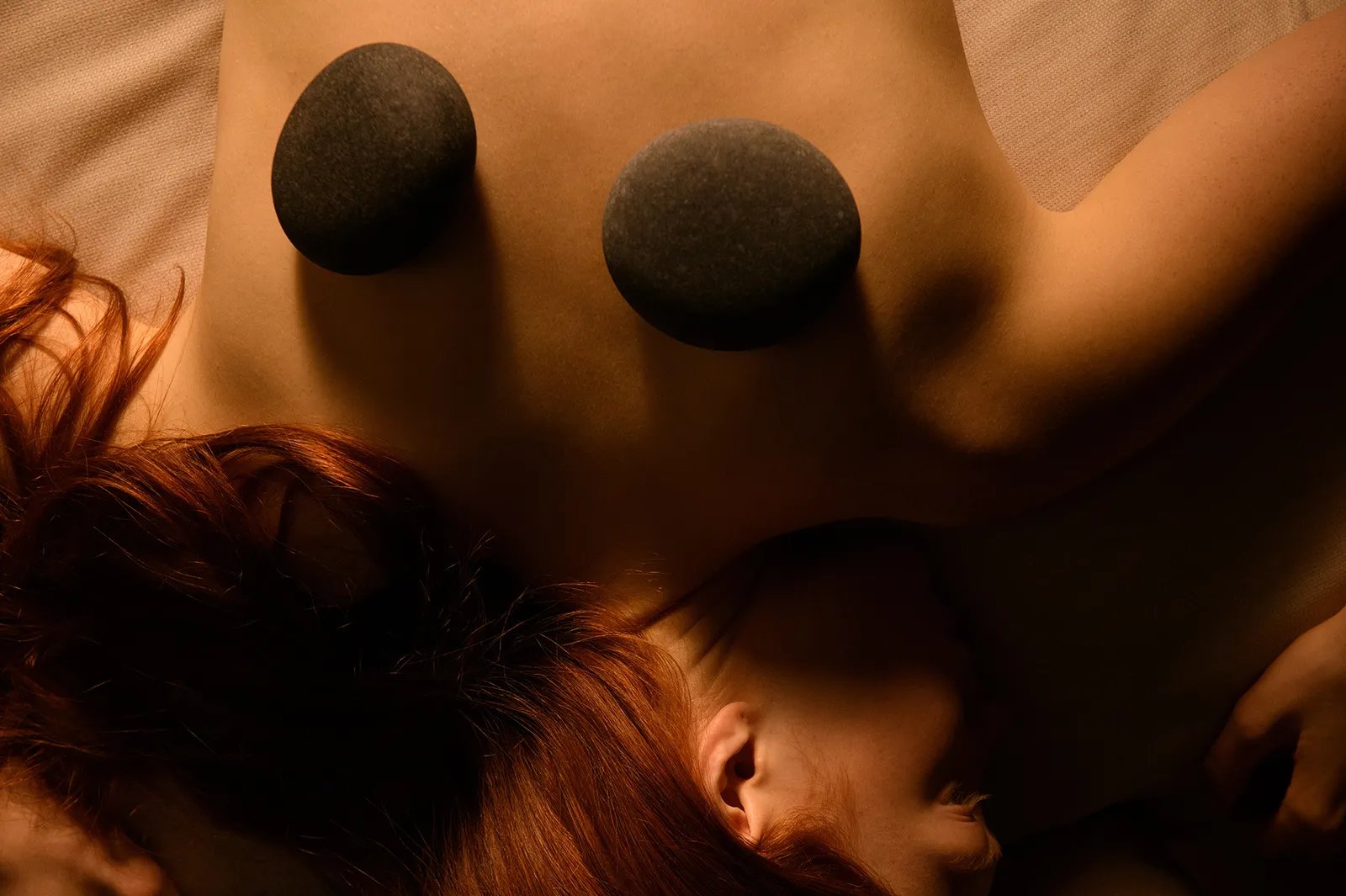 A hot-stone massage: 2 dark stones on the back of a guest lying down.