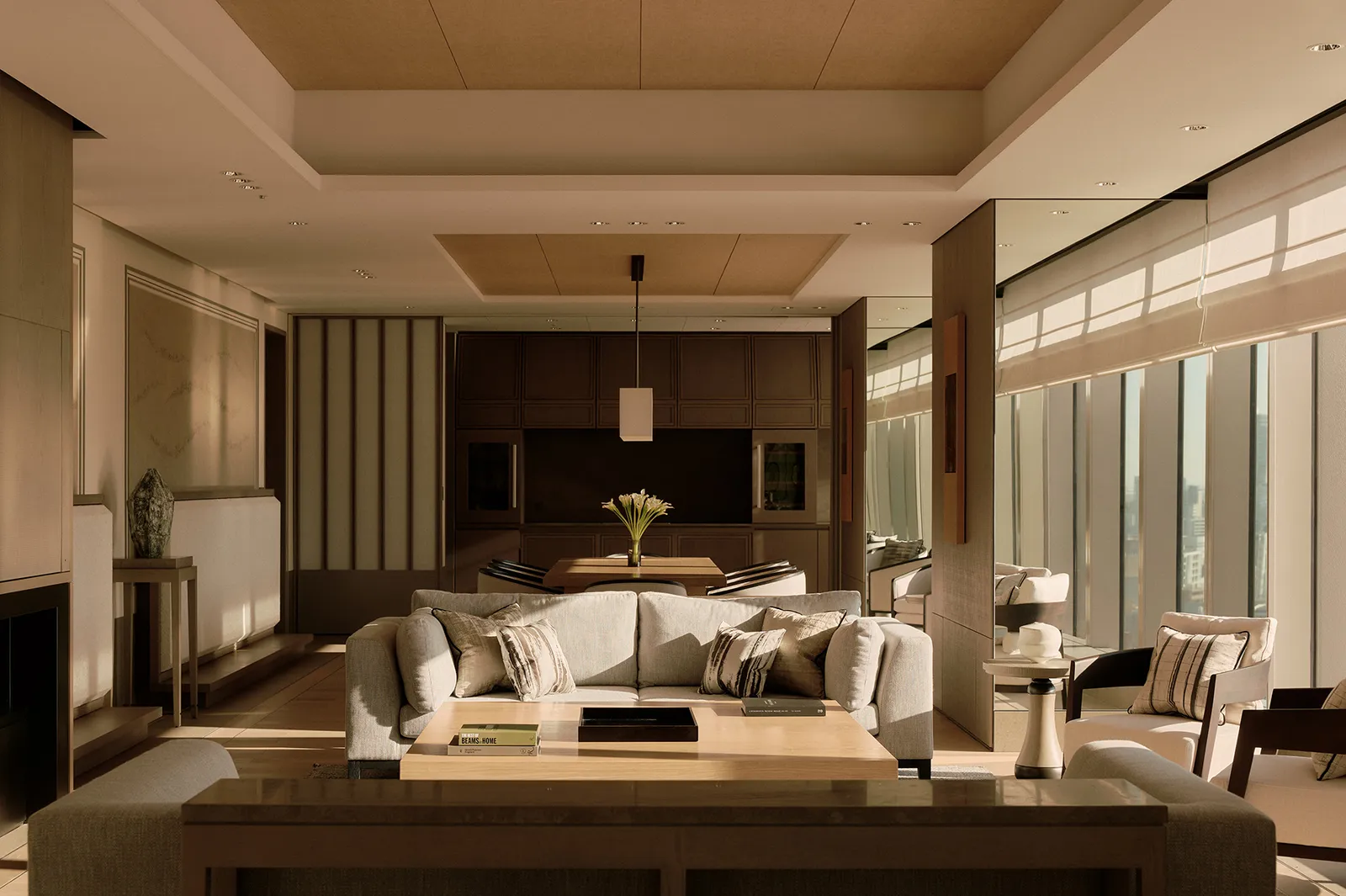 A suite living room: pale sofas, a low table, the kitchen beyond and the light from the windows.