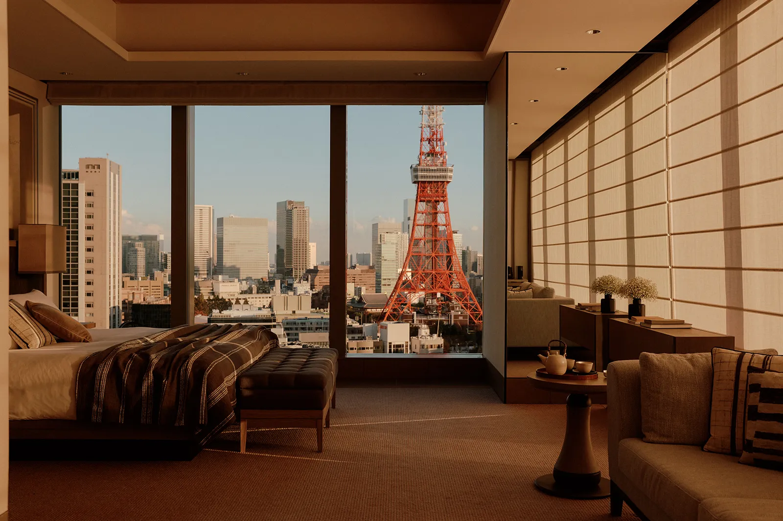 The Janu Suite bedroom at sunset, with the bed, the sofa and Tokyo Tower standing square in the window.
